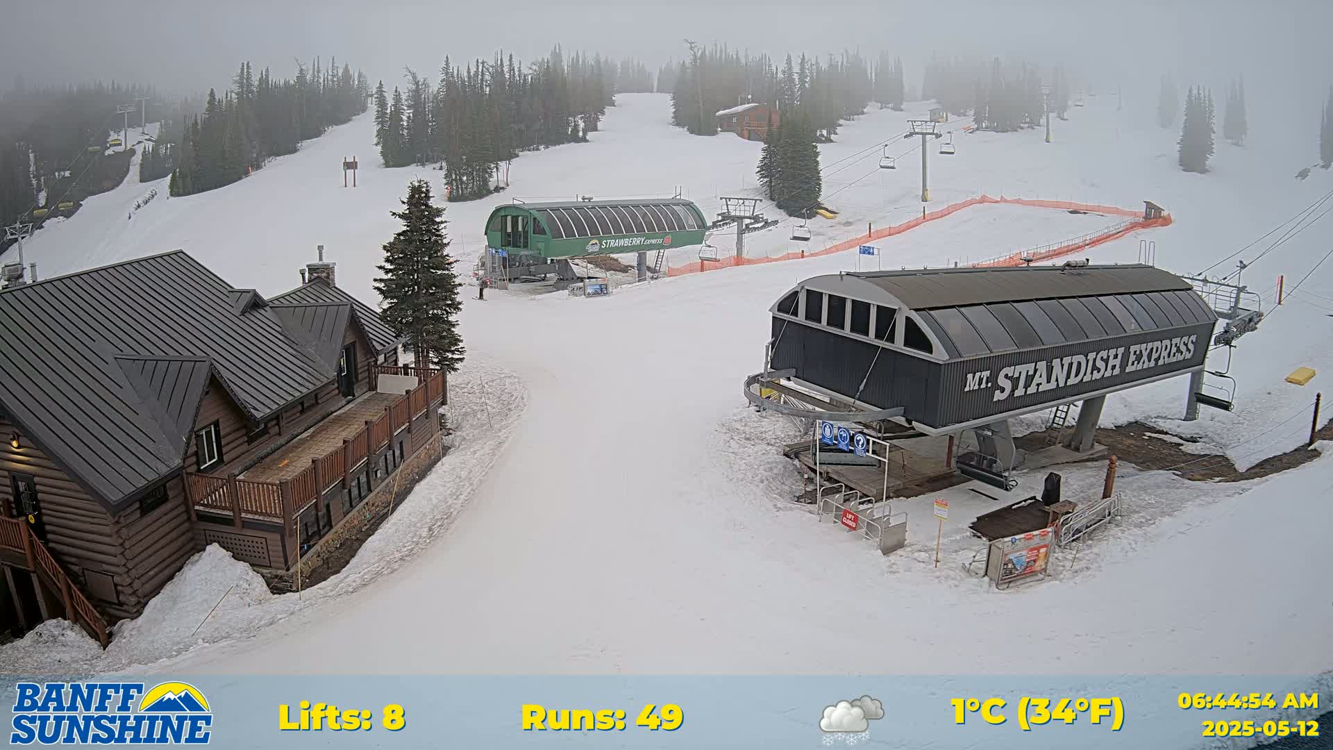 A snowy ski resort scene with two chairlifts, a lodge, and overcast skies.