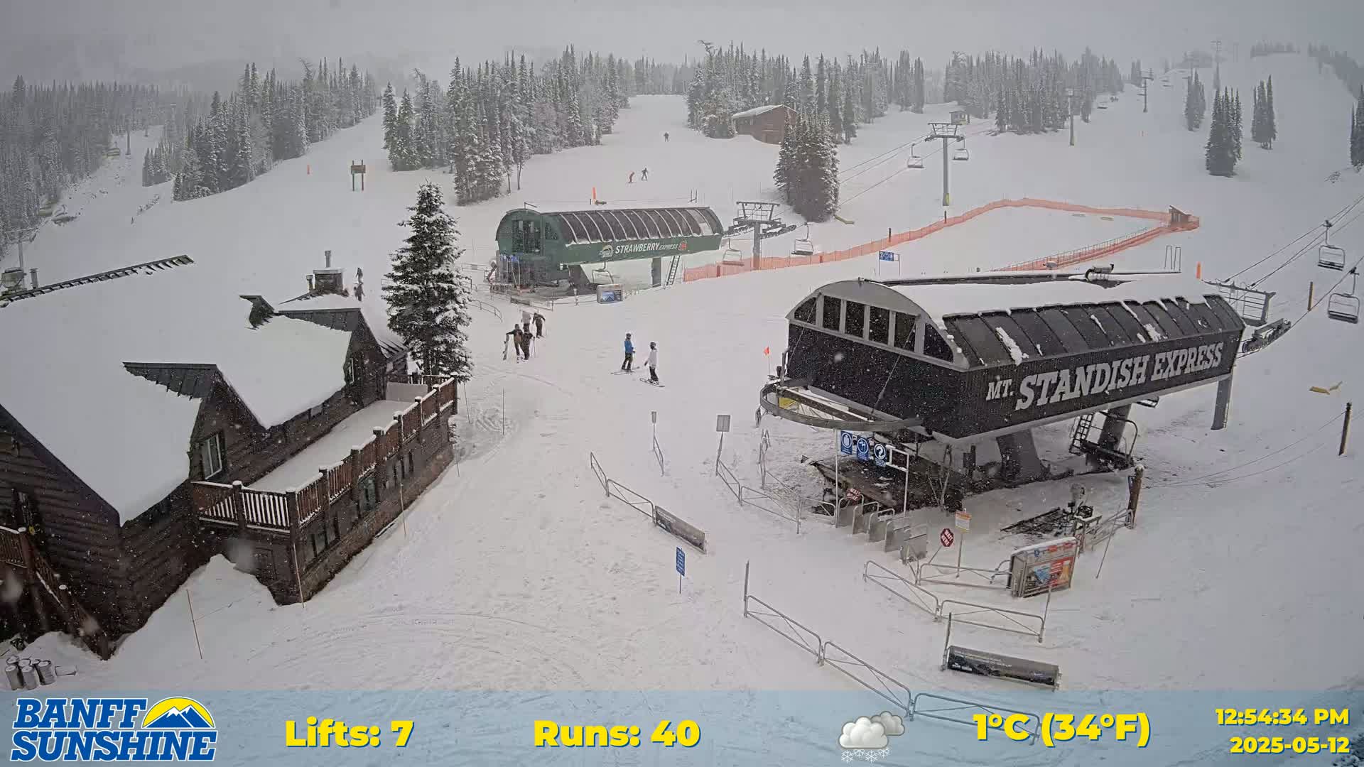 A snow-covered ski resort with several chairlifts, a lodge, and a few skiers, during a light snowfall.