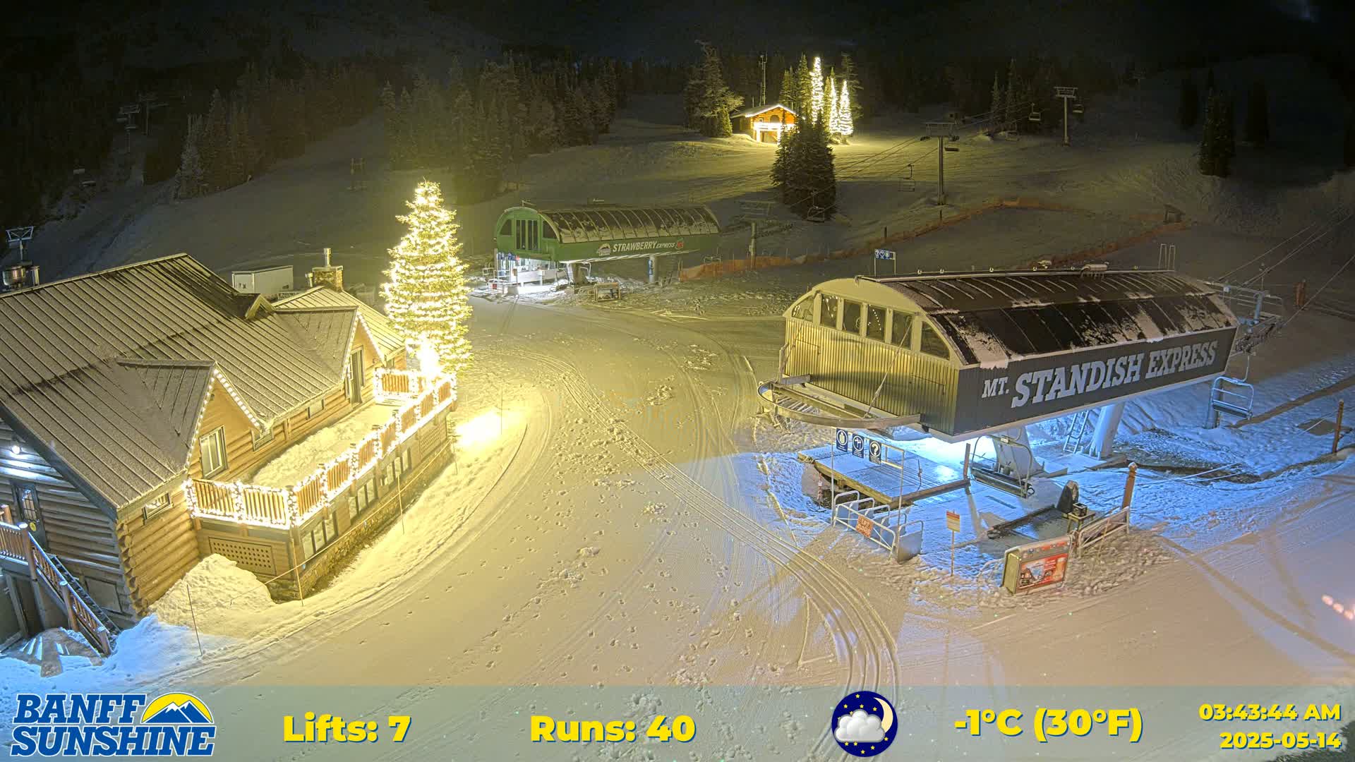A nighttime view of a snow-covered ski resort with illuminated buildings and ski lifts, under a clear, cold (-1°C) sky.