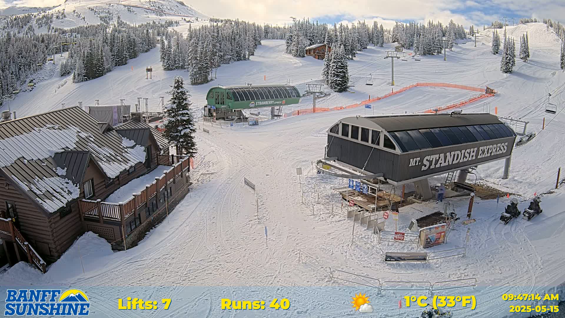 A snow-covered ski resort with two chairlifts, a lodge, and several snowmobiles is visible on a partly sunny day.