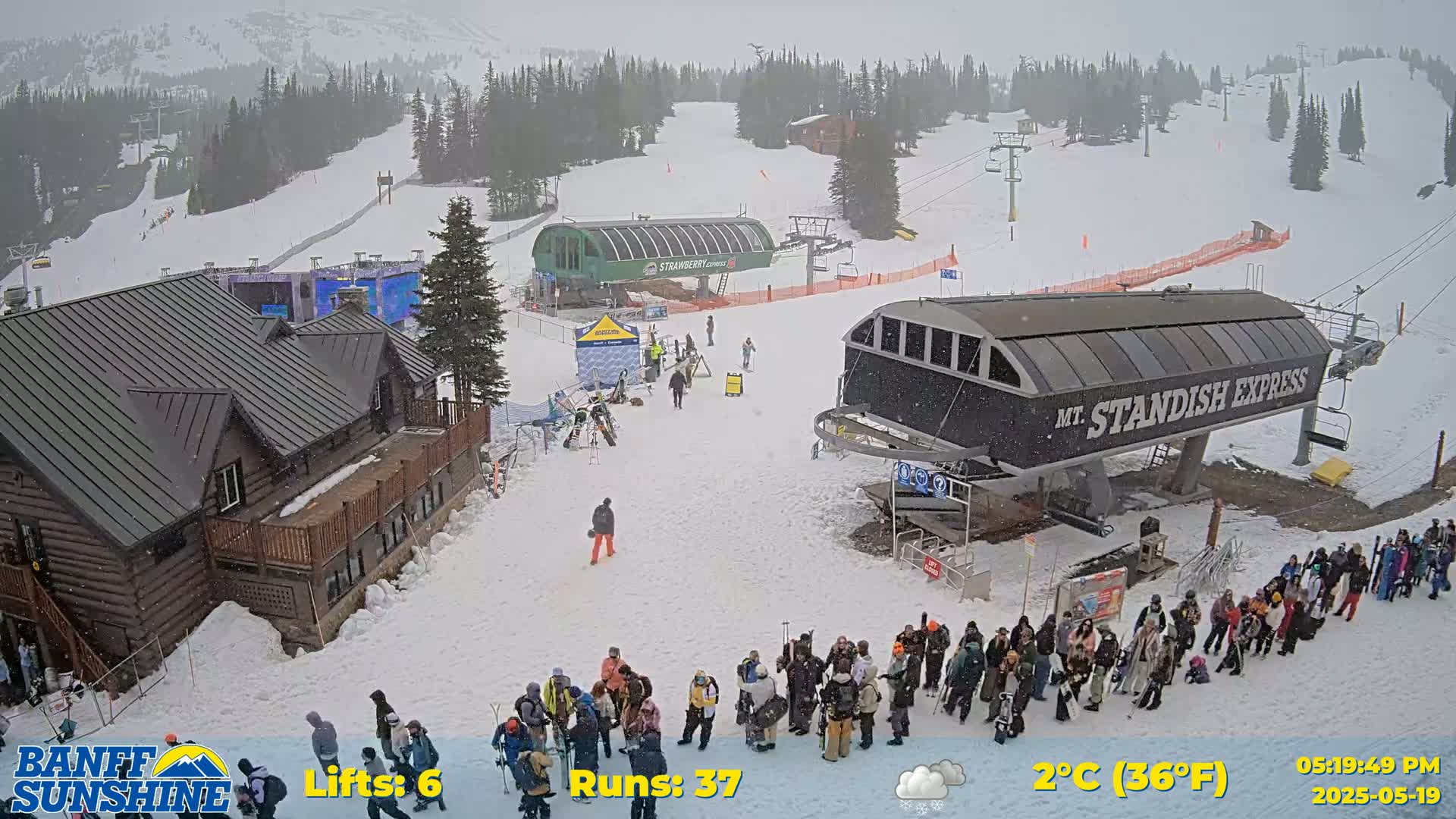 A snowy ski resort scene shows a lodge, two chairlifts, and several people waiting in lines, with light snow falling.