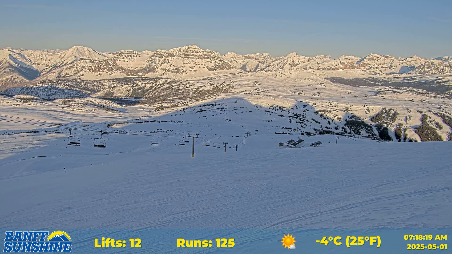 A snowy mountain range is visible in the background of a ski resort, under sunny, cold conditions.