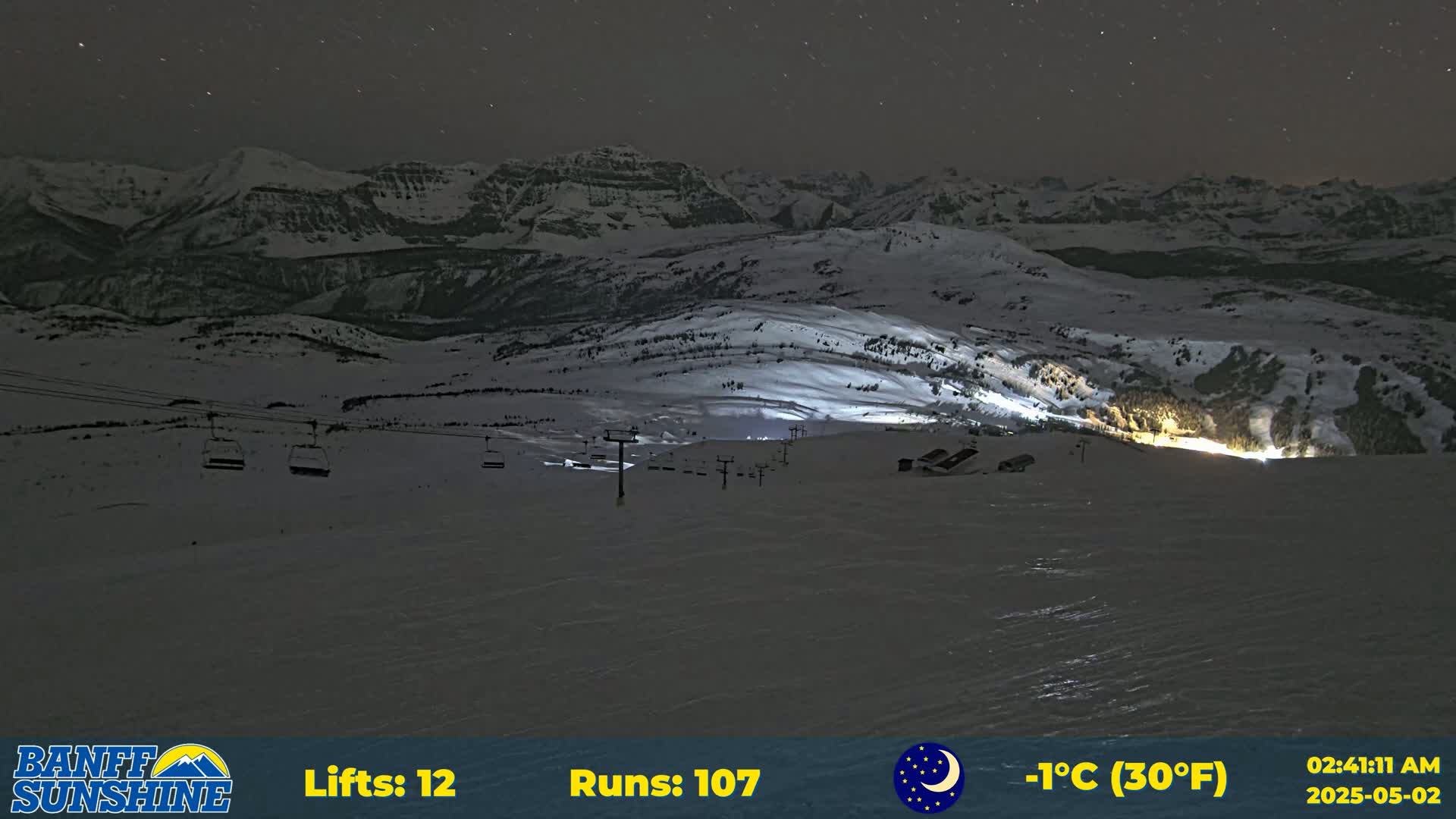 A nighttime view of a snow-covered mountain range with several ski lifts and illuminated slopes under a clear, starry sky.