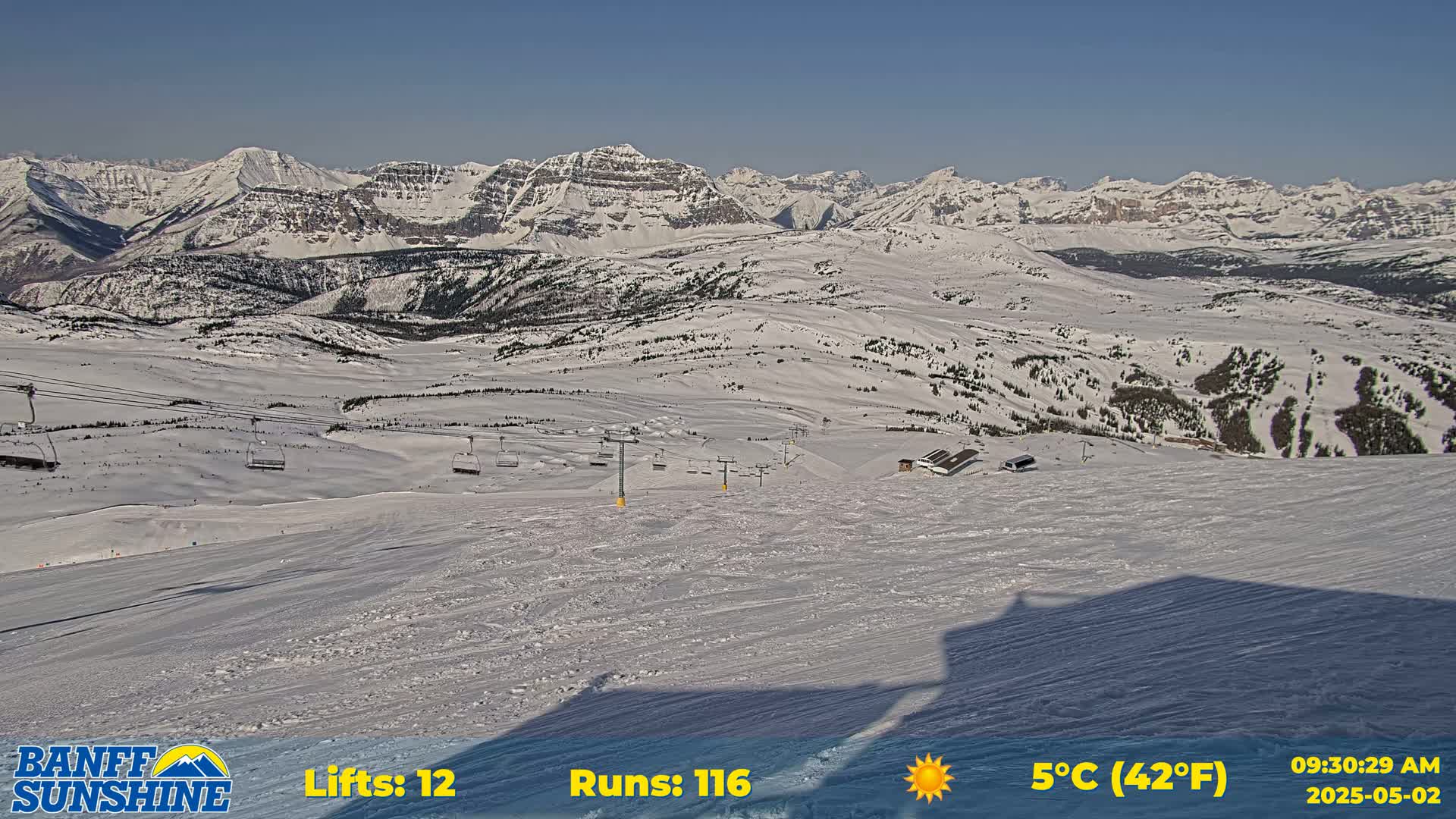 A sunny, snow-covered ski resort nestled in a mountainous region, with several ski lifts visible.