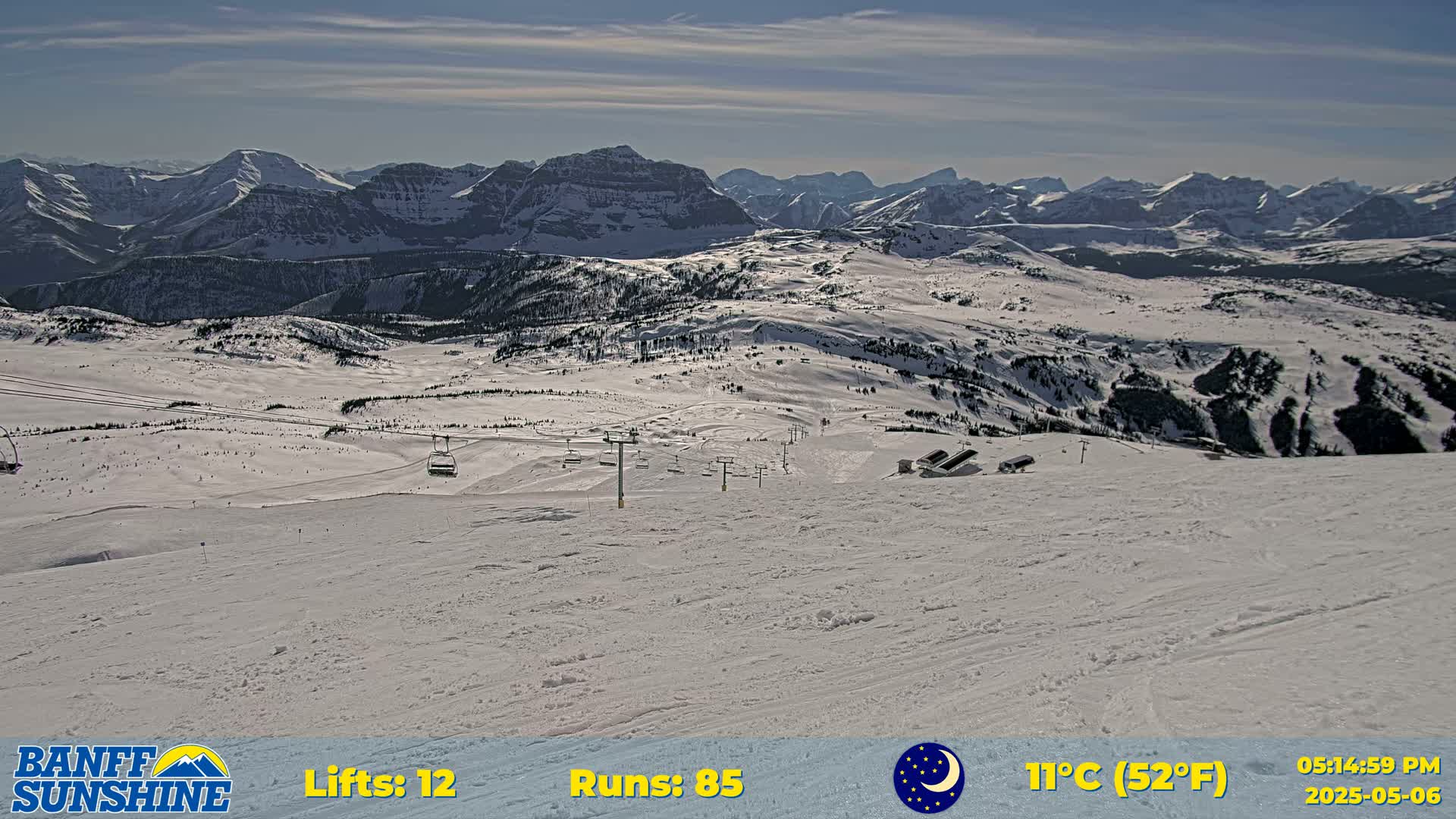 A snowy ski resort with several chairlifts and runs is visible, overlooking a vast mountain range under a mostly clear sky.