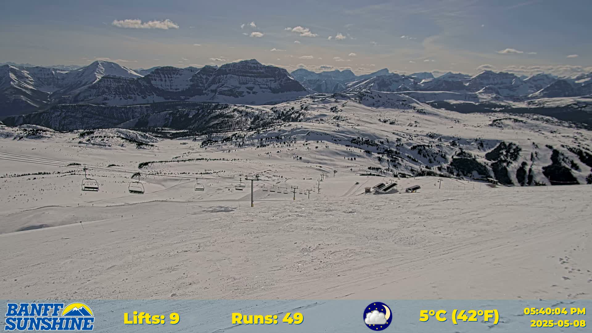 A snow-covered mountain landscape with several ski lifts and runs visible under a mostly sunny sky.