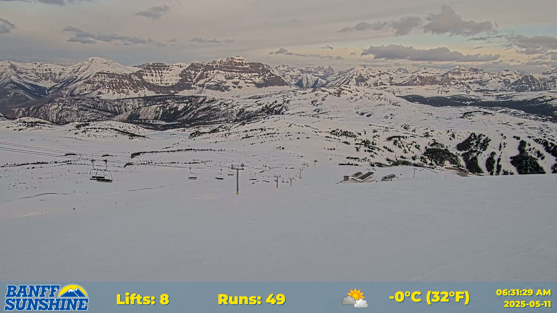 A snow-covered ski resort with several chairlifts and runs is visible against a backdrop of mountain ranges under a partly cloudy sky.