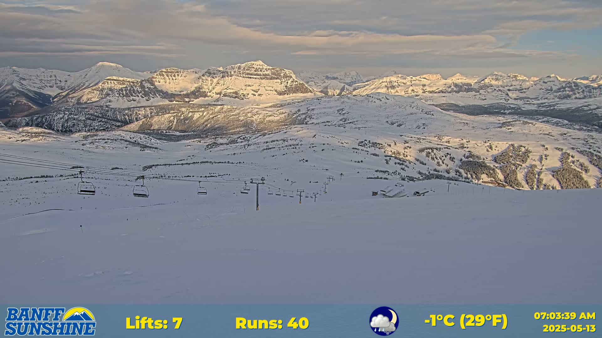 A snowy mountain ski resort at dawn with several chairlifts visible, under partly cloudy skies and a temperature of 29°F.
