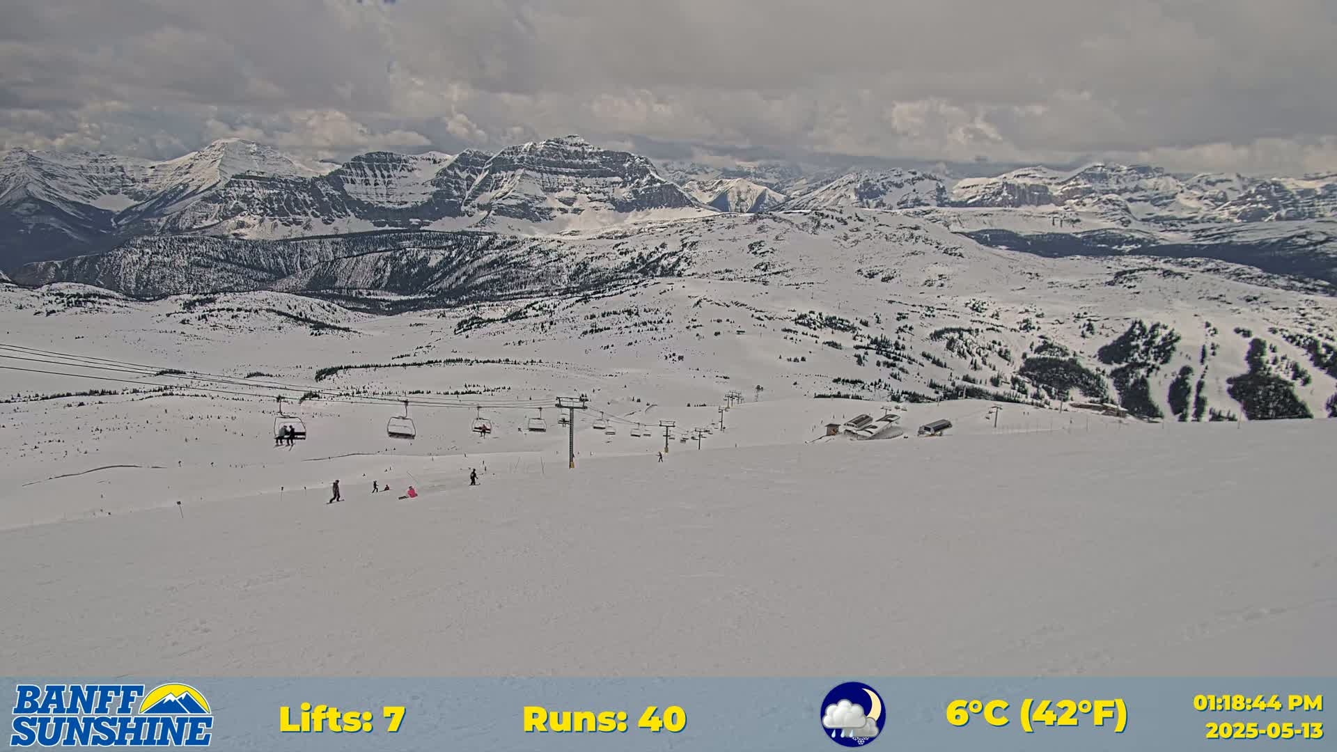 A snowy mountain ski resort with several chairlifts and a few skiers and snowboarders visible on a cloudy day.