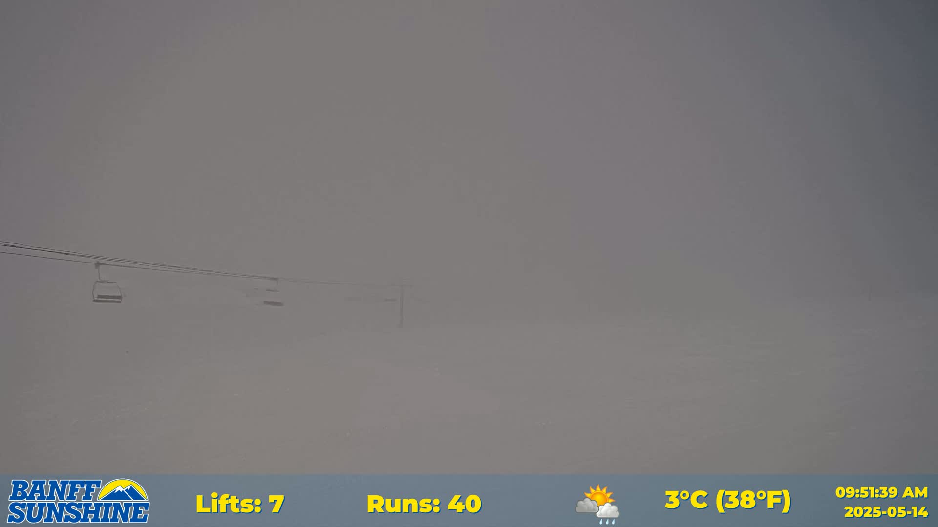 A foggy, snowy scene shows two empty chairlifts against a gray sky, with a few rain showers.
