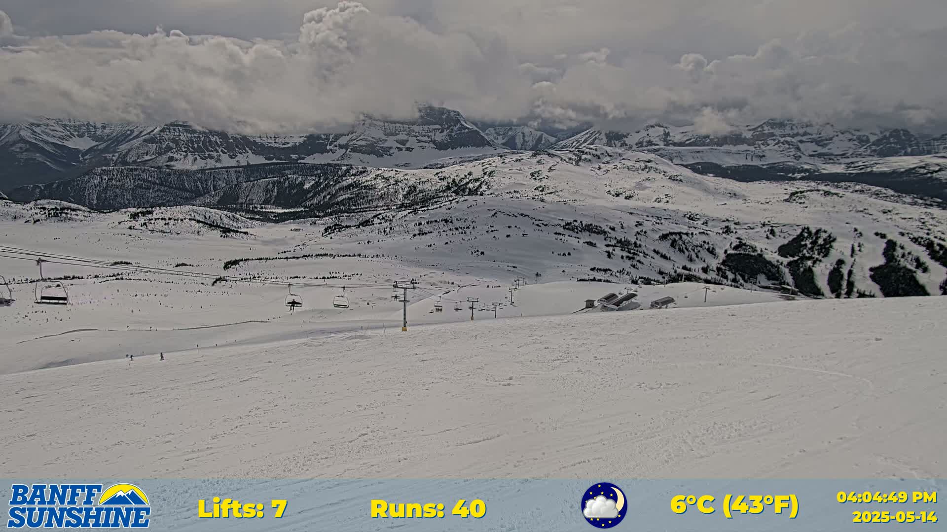 A snow-covered mountain slope with ski lifts and runs under a cloudy sky.