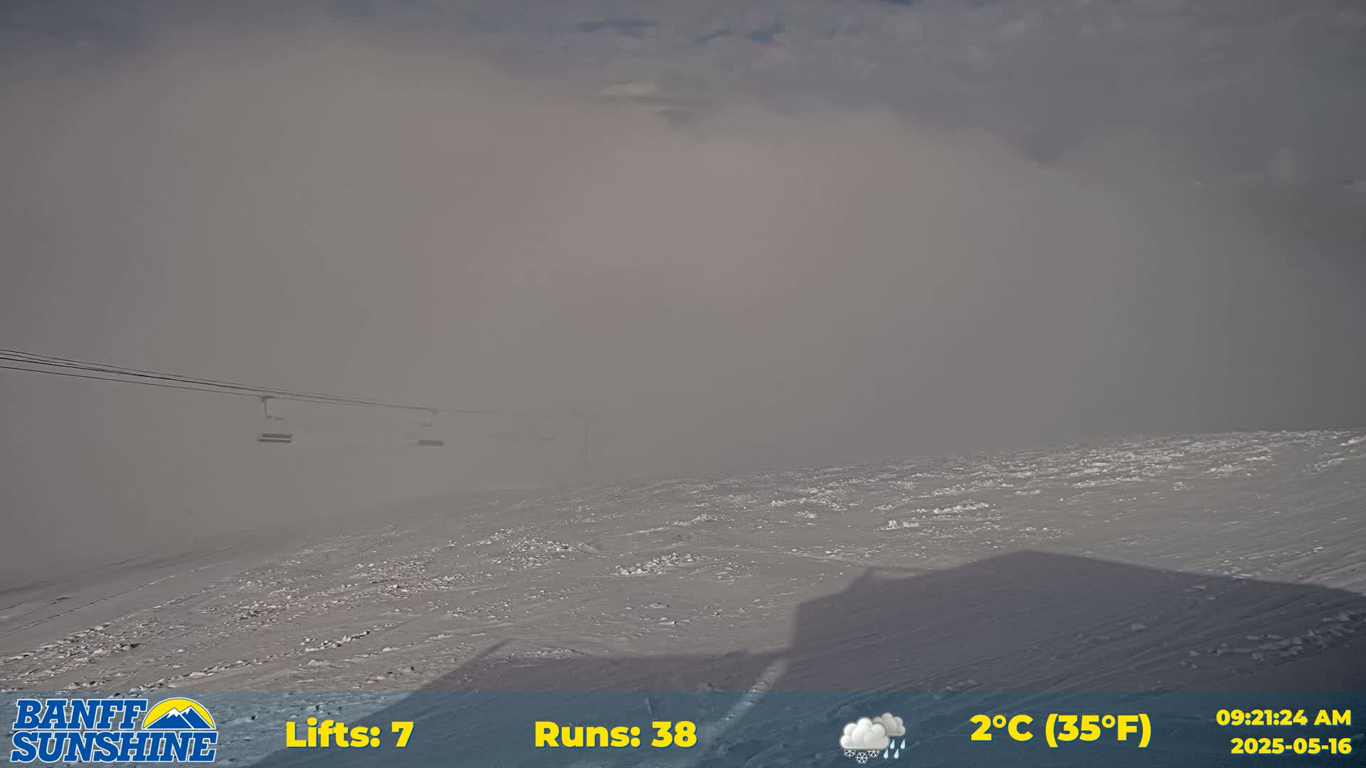 A snowy, foggy landscape with a chairlift visible in the distance under a cloudy sky.