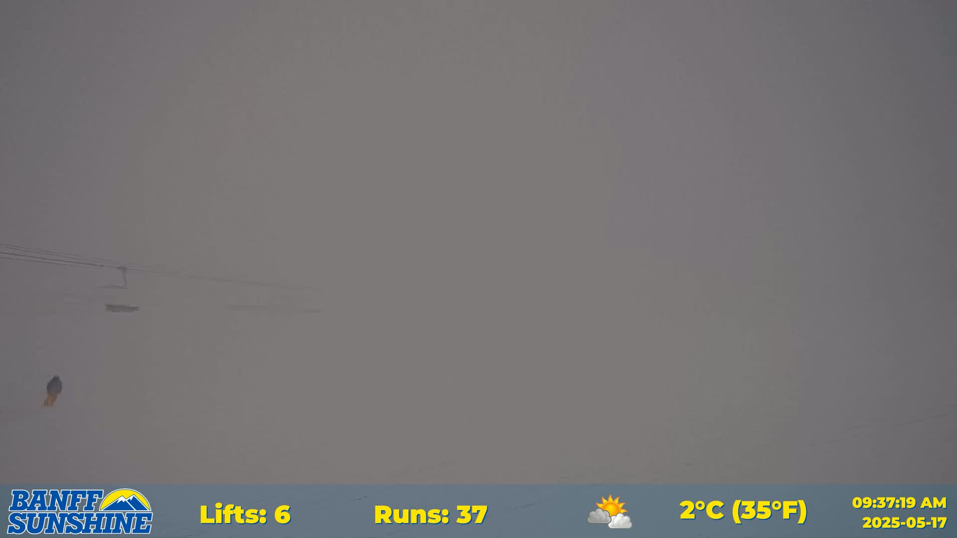 A person is visible in the distance on a snow-covered slope in foggy conditions.