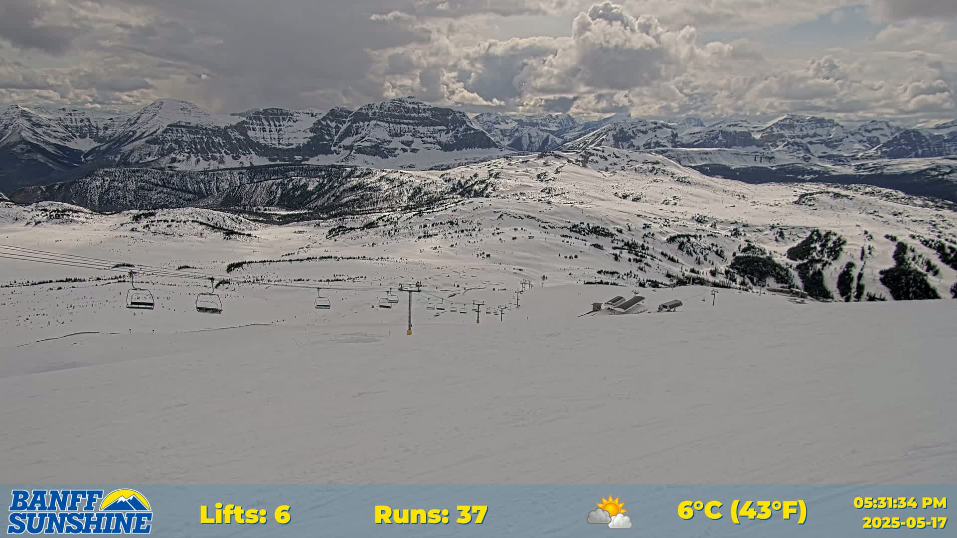 A snow-covered mountain landscape with several chairlifts and ski runs, under a partly cloudy sky.