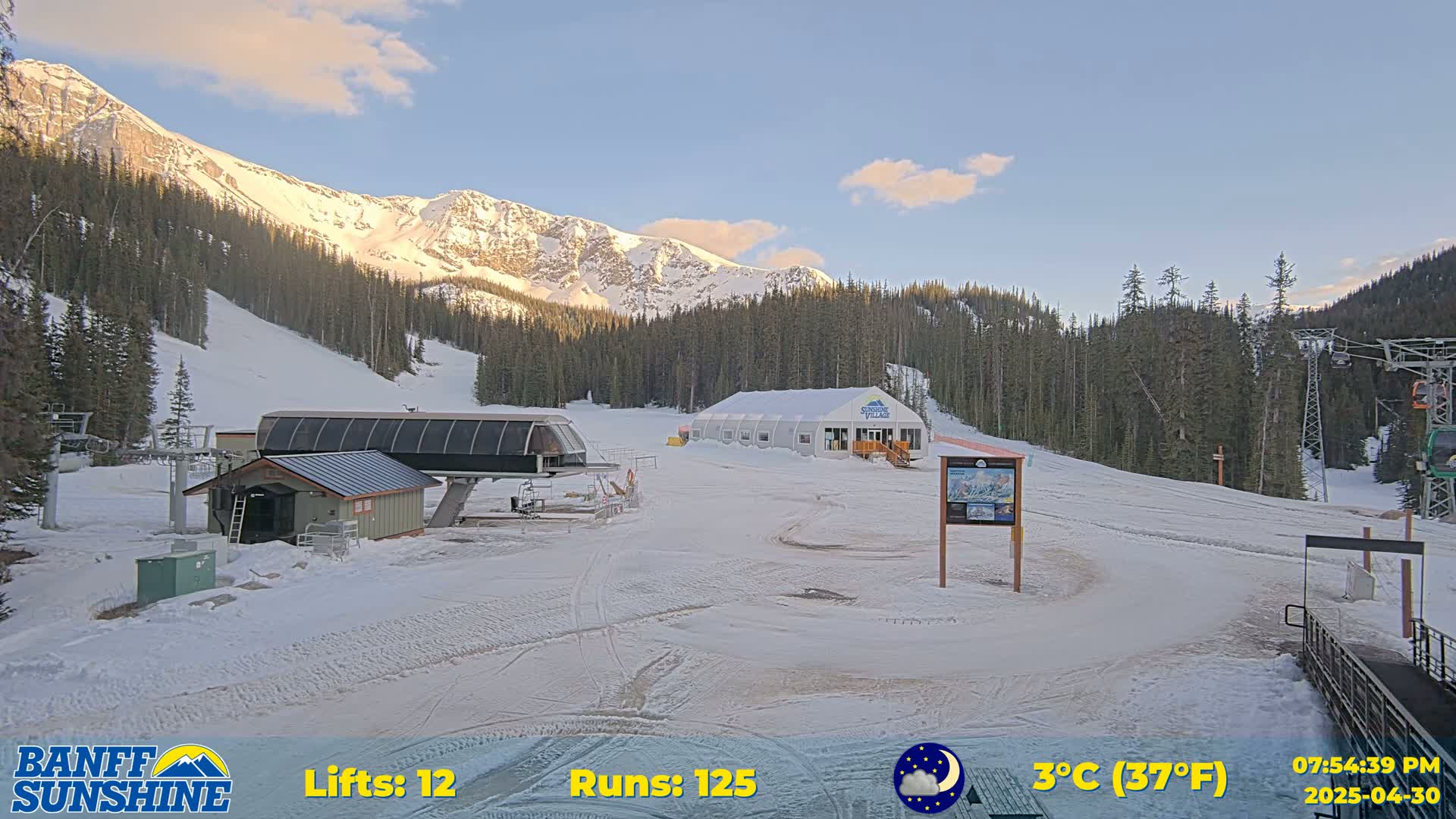 A ski resort with a chairlift, snow-covered slopes, and mountains in the background under a clear, twilight sky.