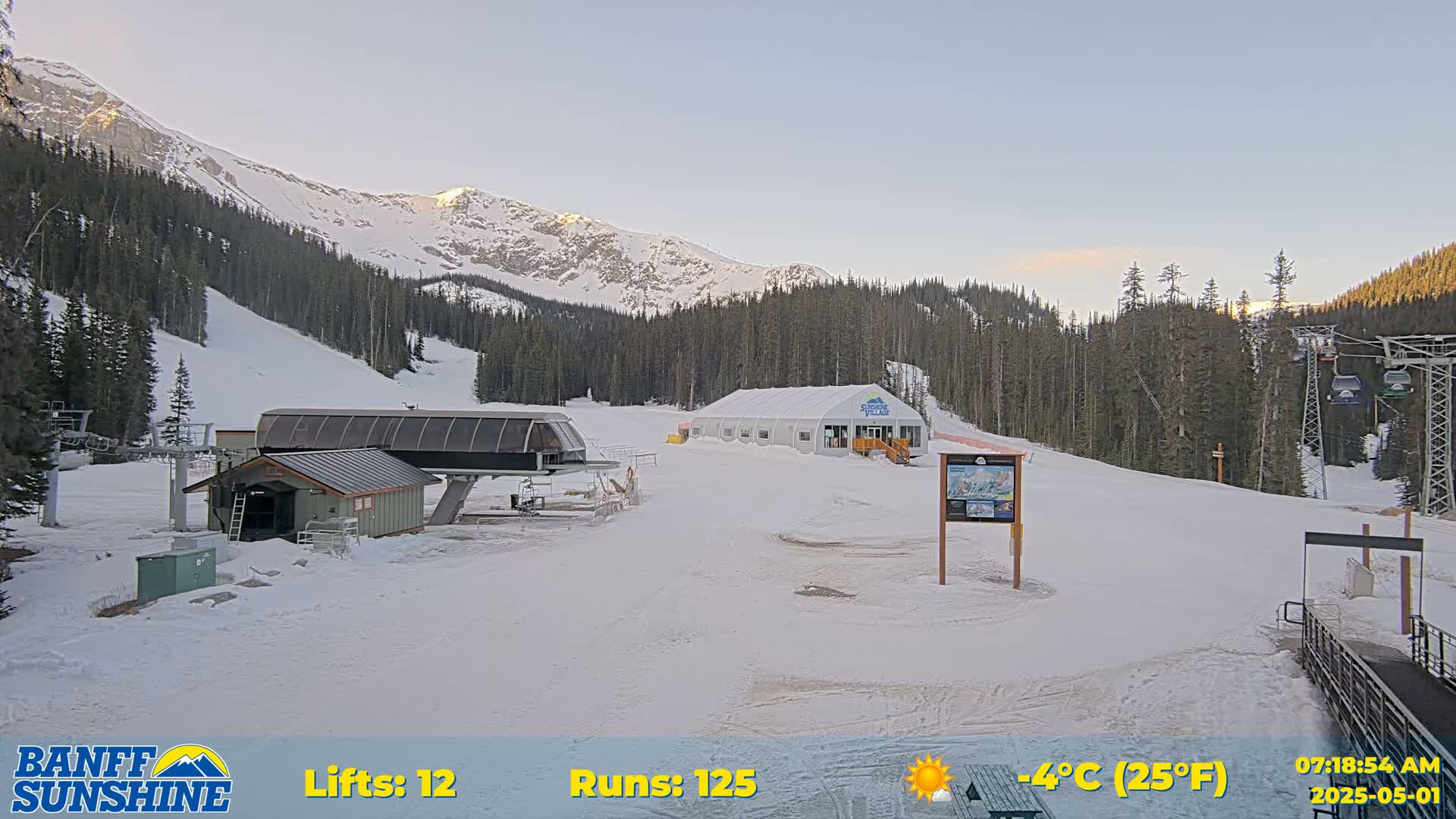 A ski resort with a chairlift, a small building, and a large tent sits on a snowy mountainside under a clear sky.