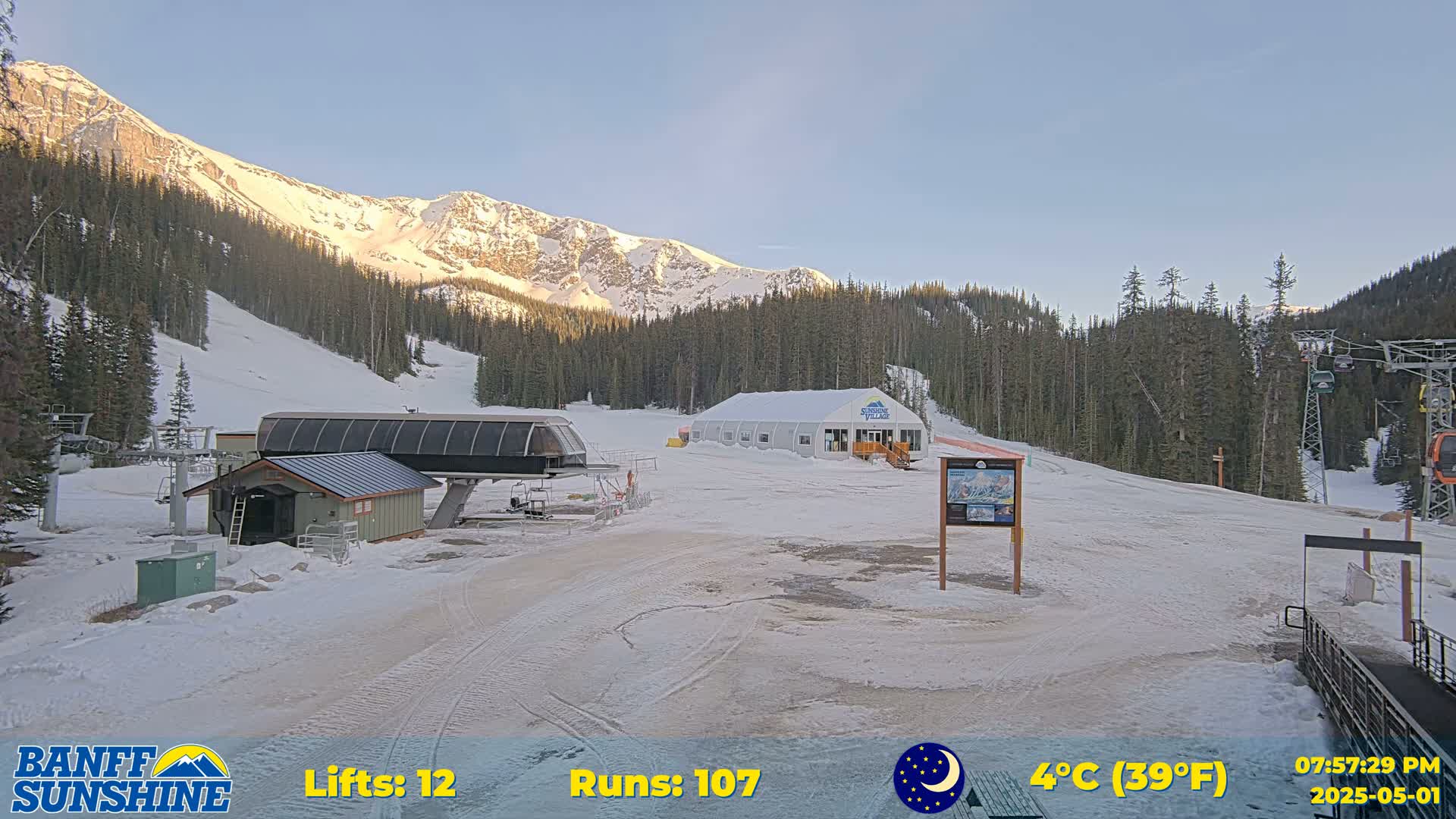 A ski resort with a chairlift, a small building, and a snow-covered landscape under a clear, bright sky.