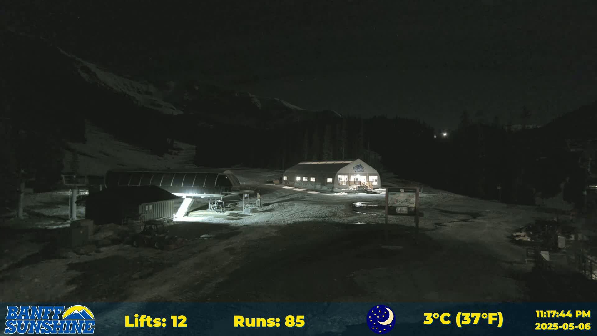 A nighttime view of a ski resort with a building and ski lift illuminated, under a clear, cold sky.
