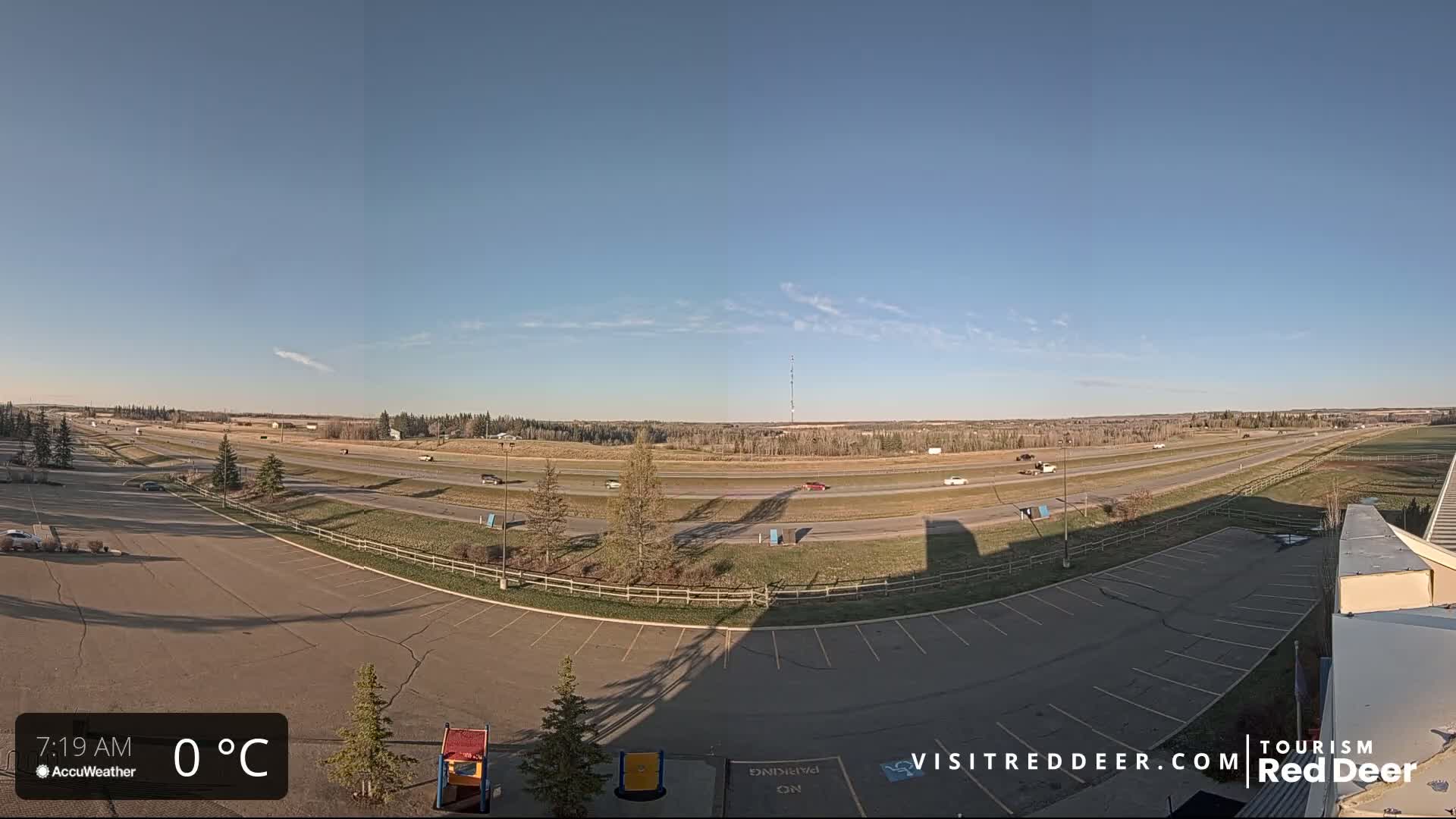 A mostly empty parking lot overlooks a multi-lane highway with sparse traffic under a clear, sunny sky.