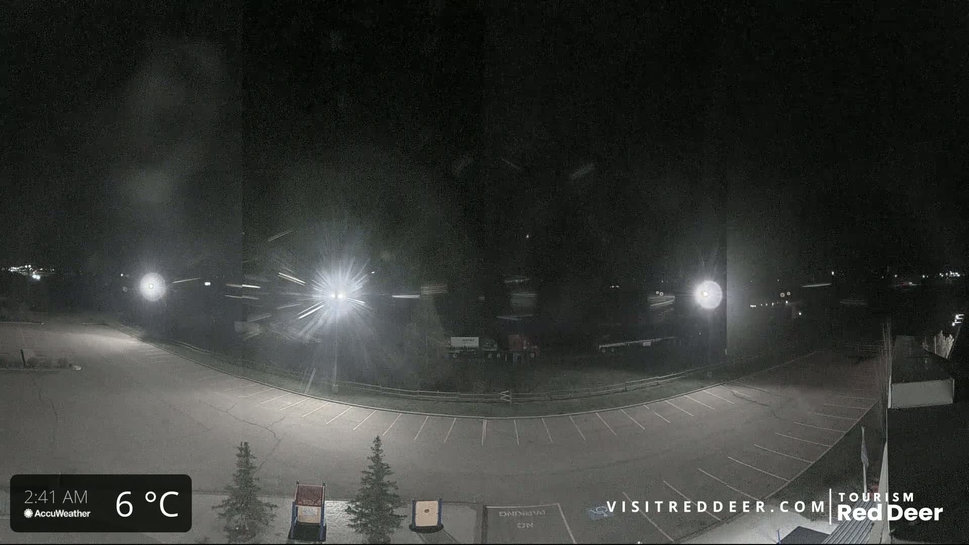A nighttime view of an empty parking lot with light snow falling under bright lights.