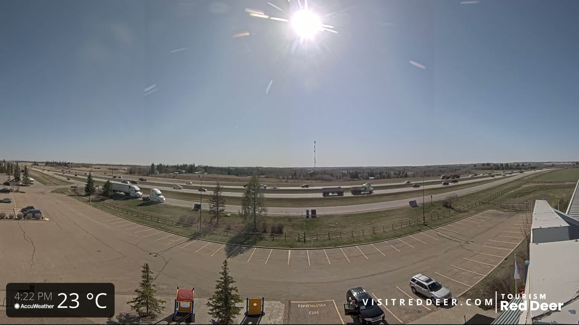 A sunny, 23°C day shows a highway with moderate traffic and an adjacent parking lot with a few cars.