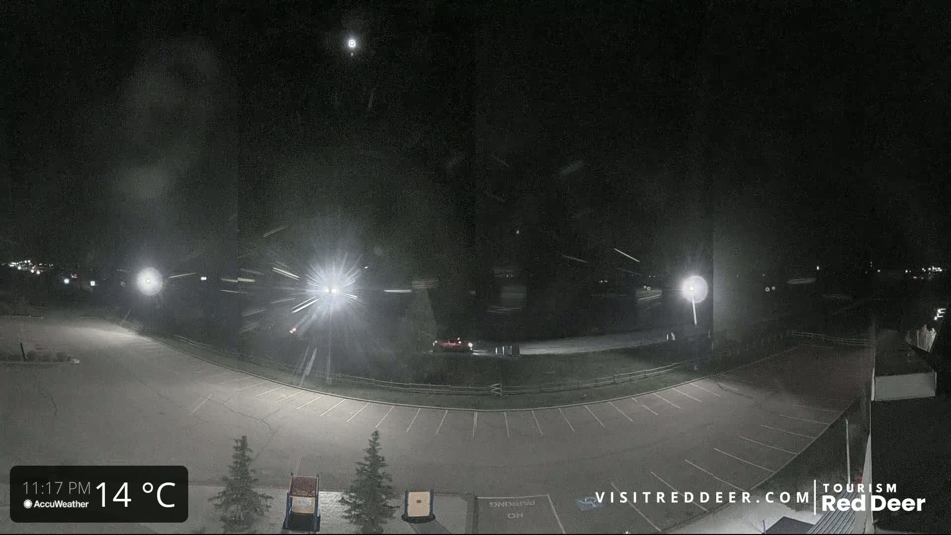 A nighttime view of an empty parking lot with light snow falling under a dark sky.