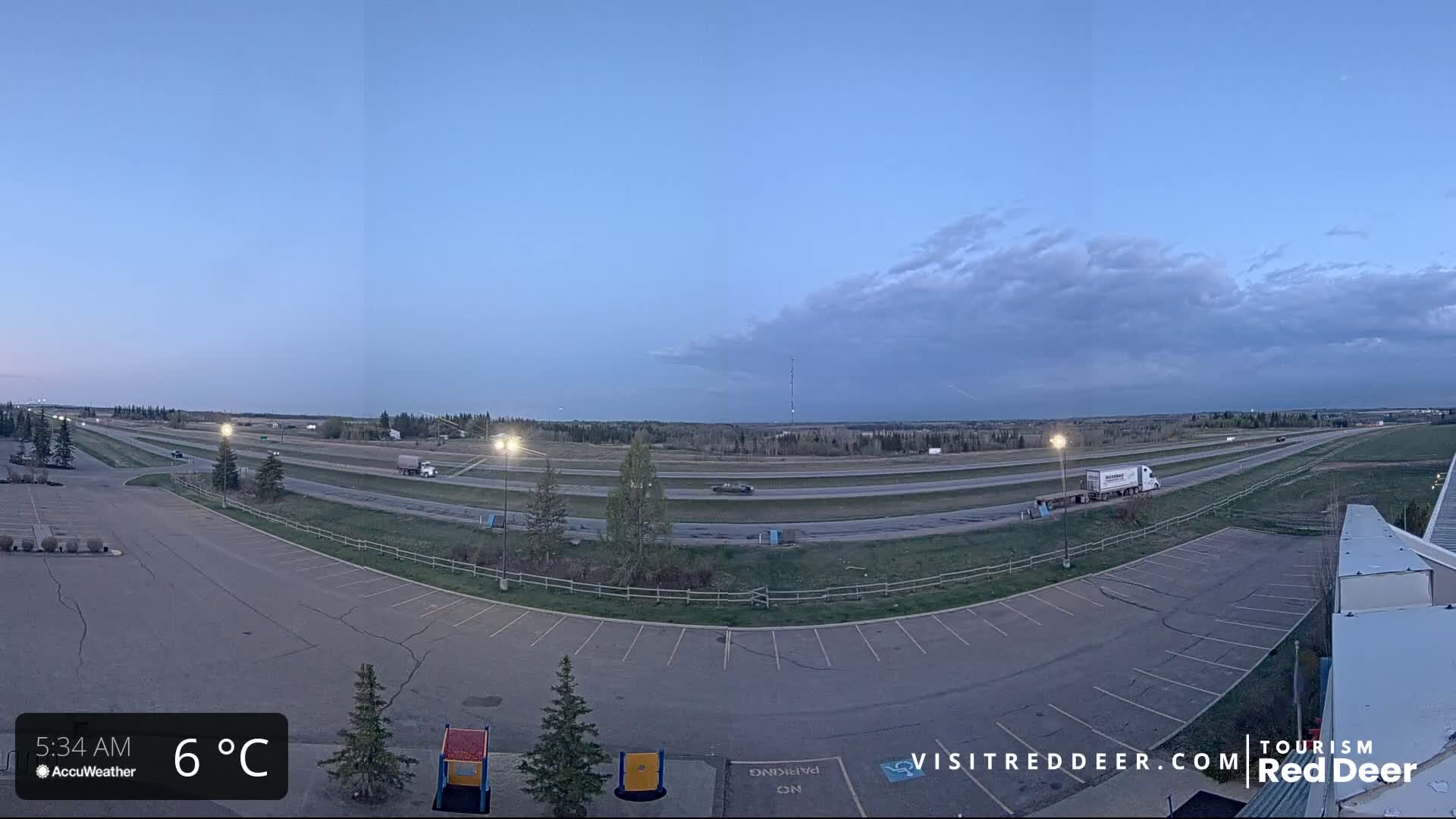 A mostly empty parking lot overlooks a multi-lane highway under a partly cloudy, twilight sky.