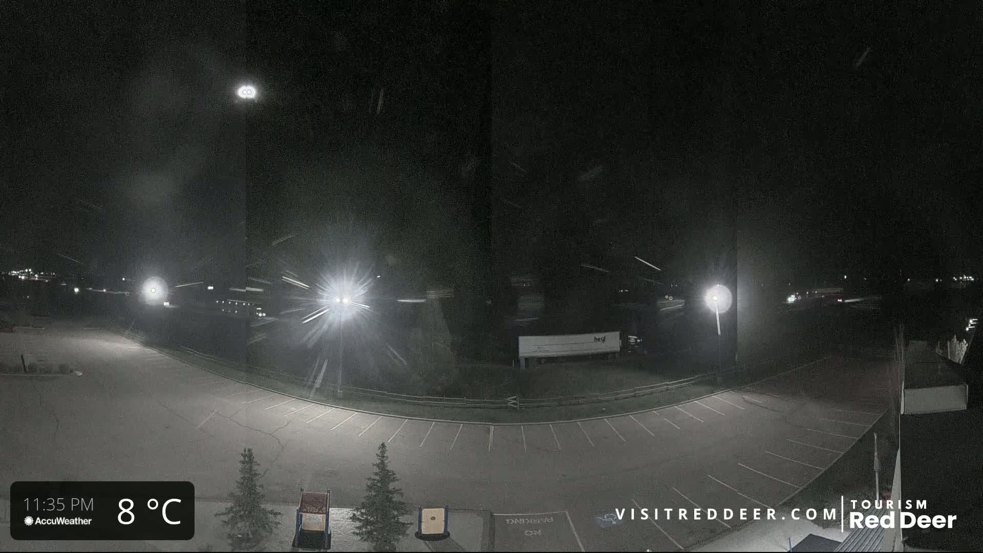 A nighttime view of a mostly empty parking lot with light snowfall and a few vehicles visible in the distance.