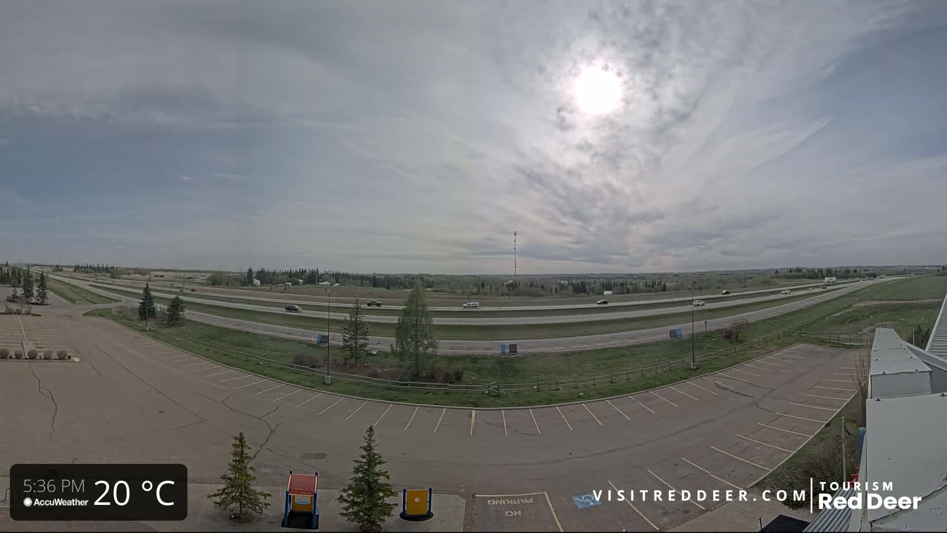 A mostly sunny day with partly cloudy skies shows a highway with sparse traffic next to an empty parking lot.