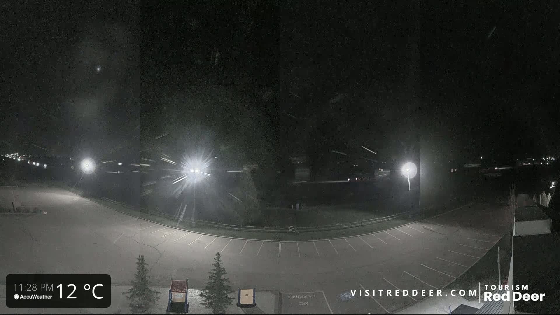 A nighttime view of a mostly empty parking lot with light snow falling under bright artificial lights.