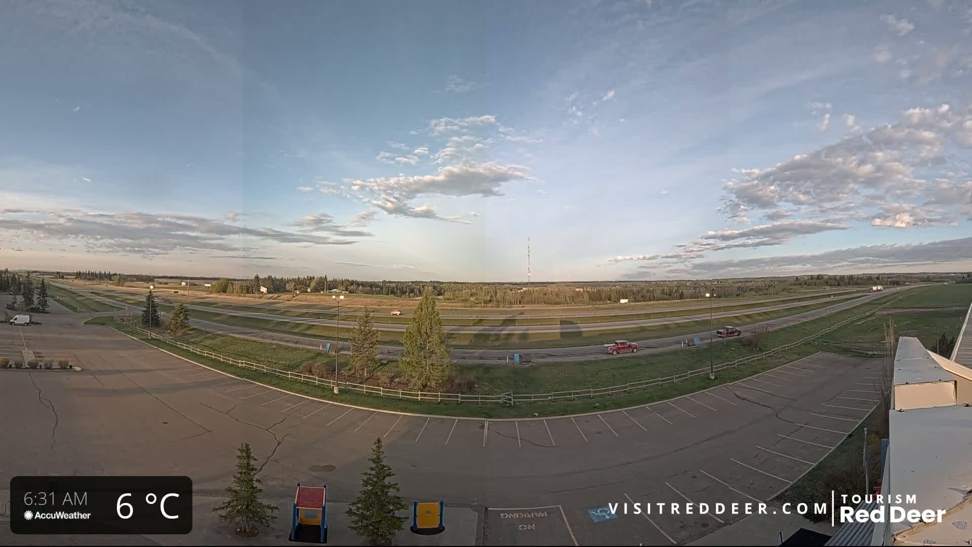 A mostly empty parking lot overlooks a highway and a flat landscape under a partly cloudy sky.