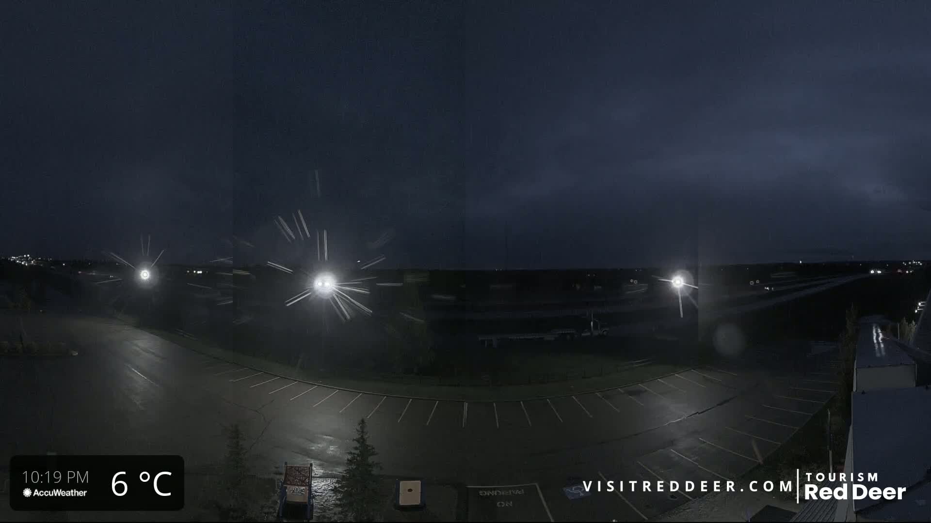 A nighttime view of a wet parking lot with several lights visible, under a dark, possibly stormy sky.