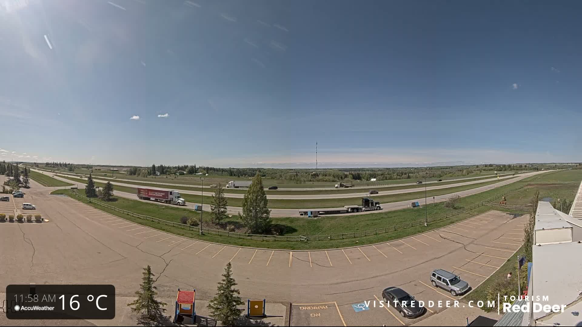 A mostly empty parking lot overlooks a multi-lane highway with several vehicles, under a clear, sunny sky.