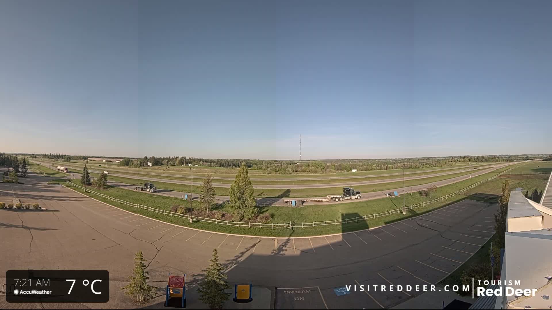 A mostly empty parking lot overlooks a multi-lane highway on a clear, sunny day with a temperature of 7°C.