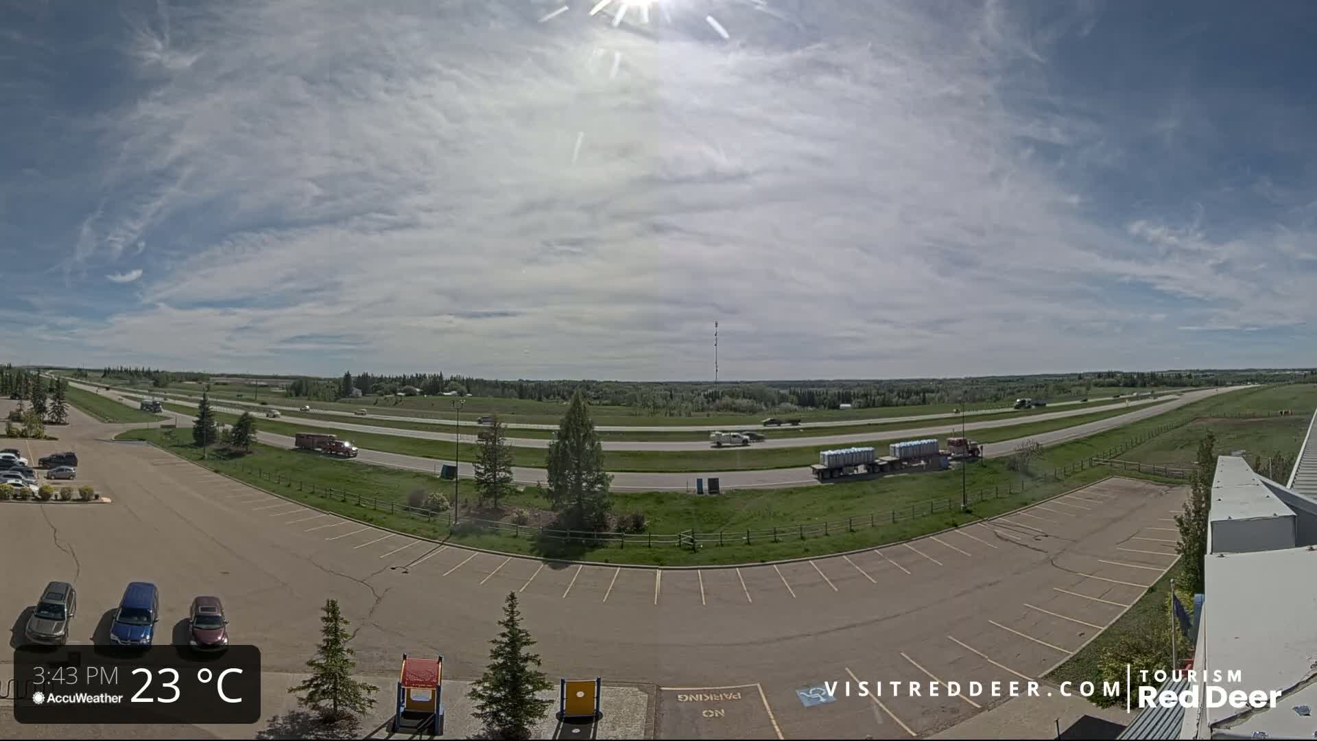 A partly sunny day shows a highway with several vehicles, including semi-trucks, and an empty parking lot with a few cars.
