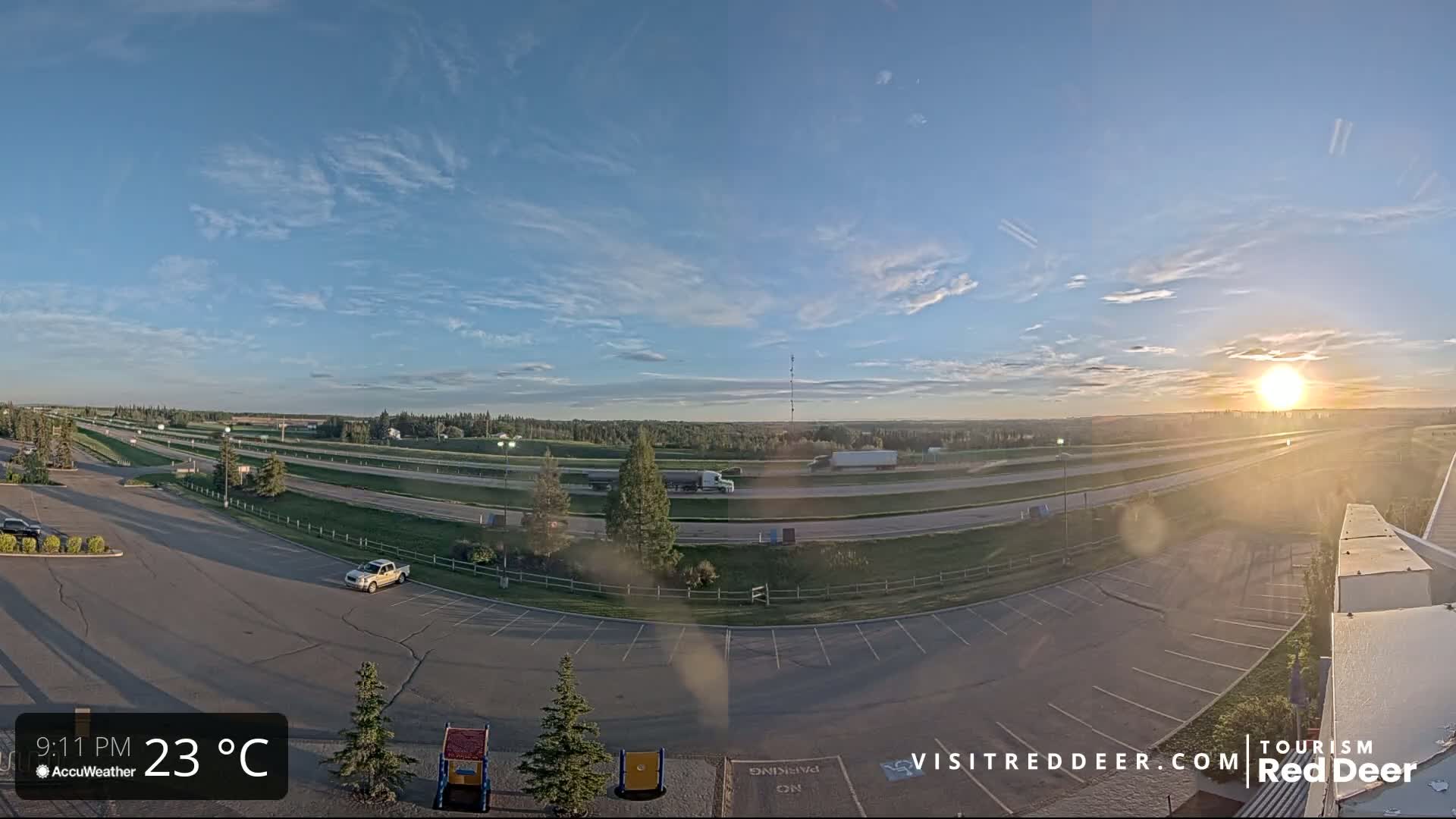 An empty parking lot overlooks a highway with a few vehicles visible under a partly cloudy sunset sky.