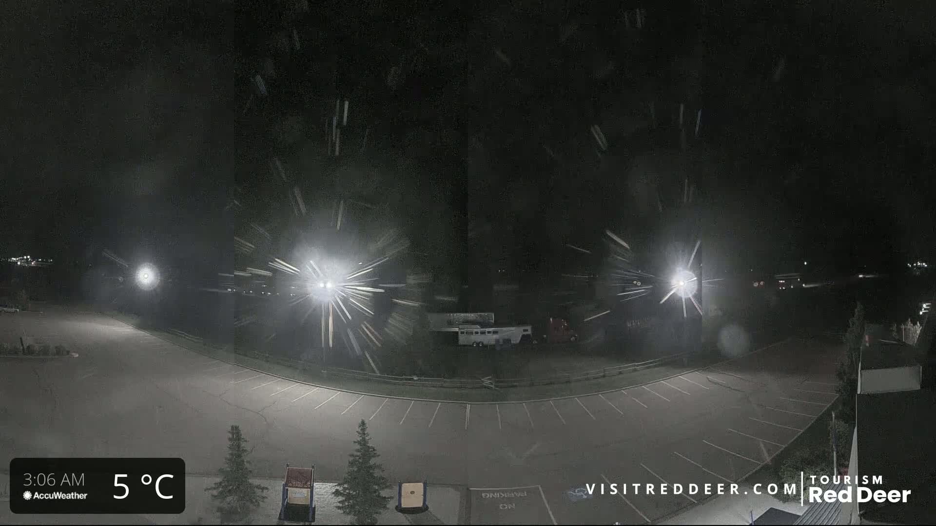 A nighttime view of a mostly empty parking lot with light snow falling under bright lights.