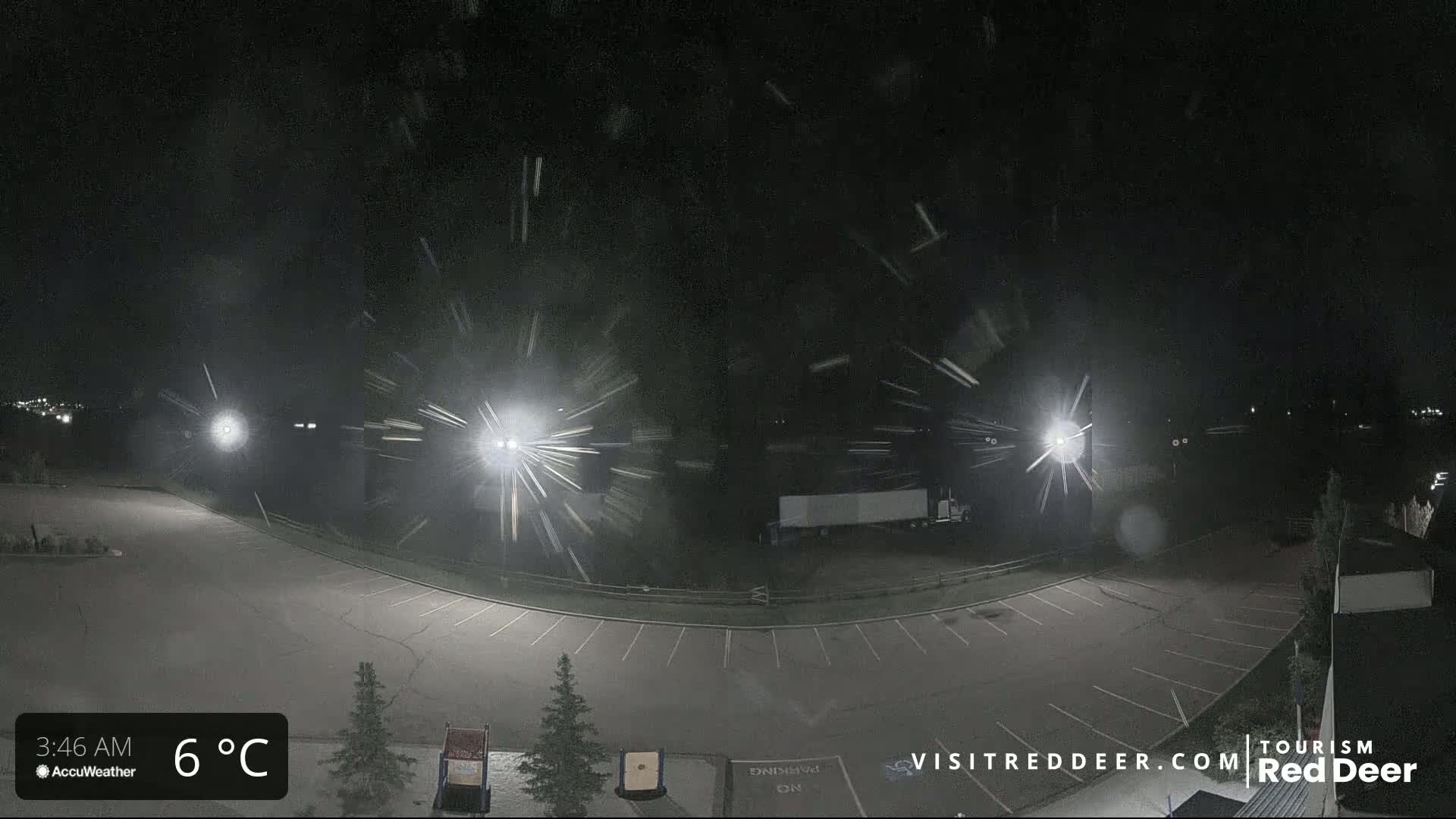 A nighttime view of a snow-covered parking lot illuminated by bright lights.