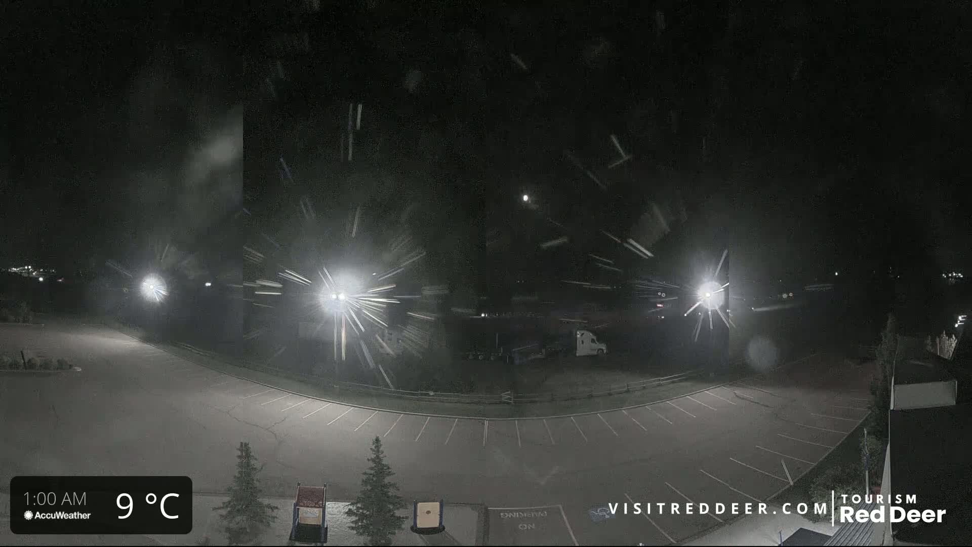 A nighttime view of a snow-covered parking lot illuminated by bright lights under a falling snow.