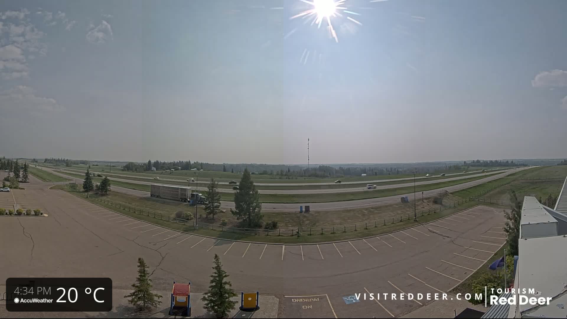 A sunny, 20°C day shows a mostly empty parking lot next to a highway with sparse traffic and a flat landscape beyond.