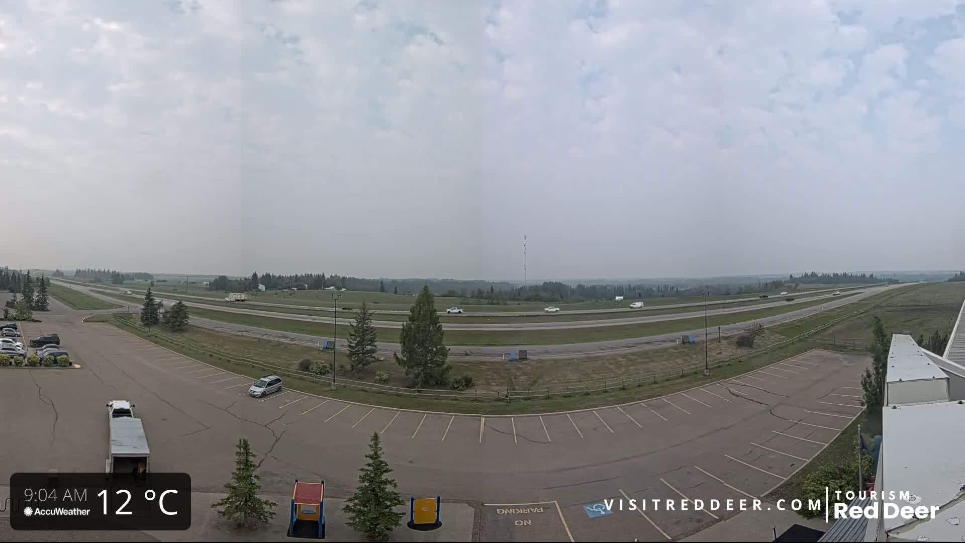 A mostly empty parking lot overlooks a divided highway with sparse traffic under a hazy, overcast sky.