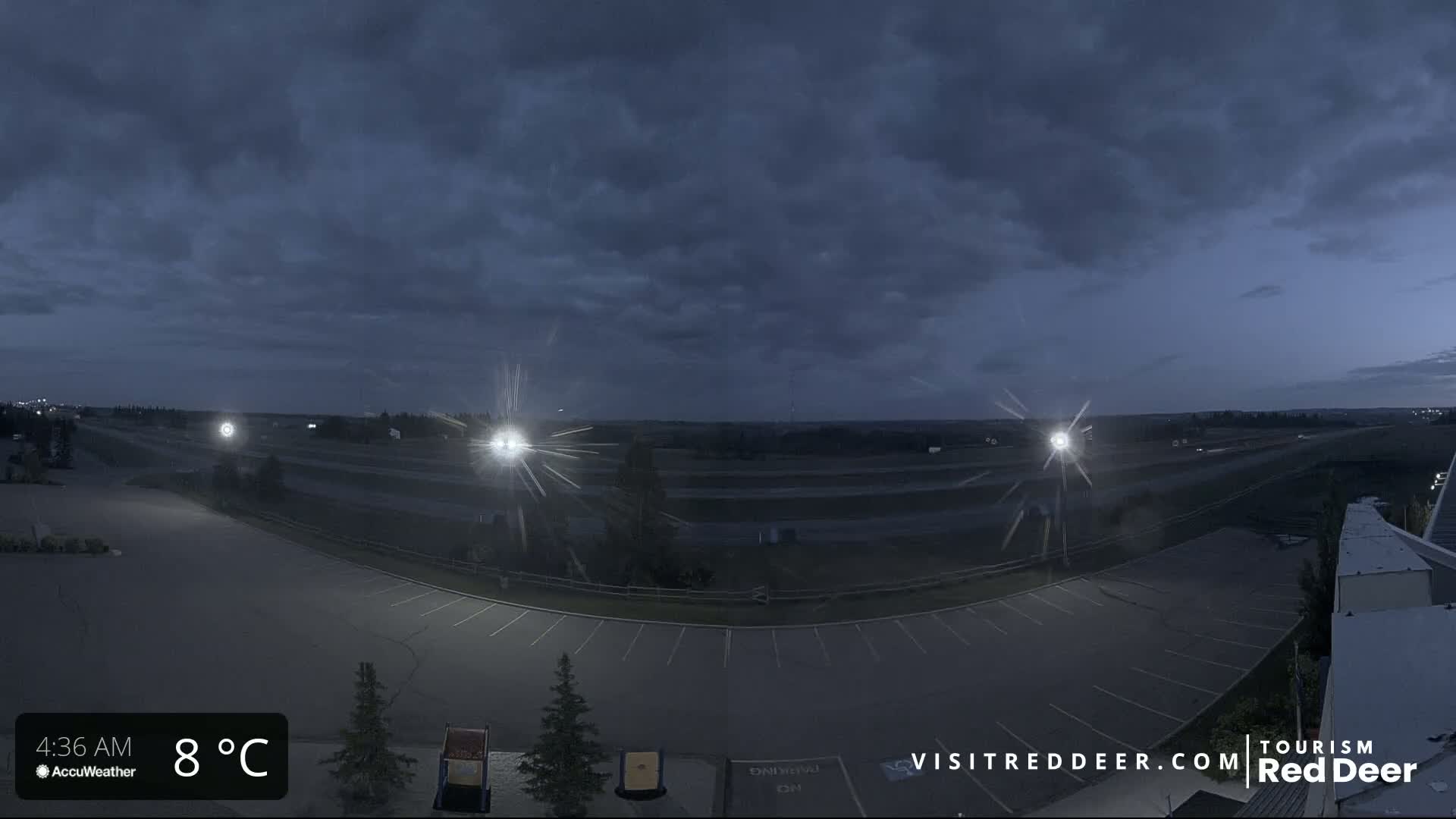 A mostly empty parking lot overlooks a highway under a dark, cloudy sky at 8°C.