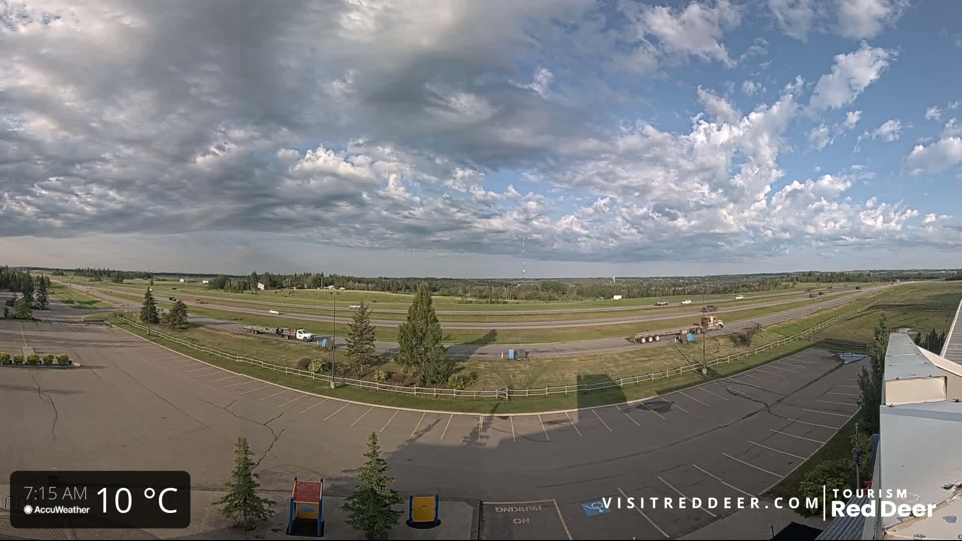 A partly cloudy sky overlooks a highway and empty parking lot with a few vehicles visible.
