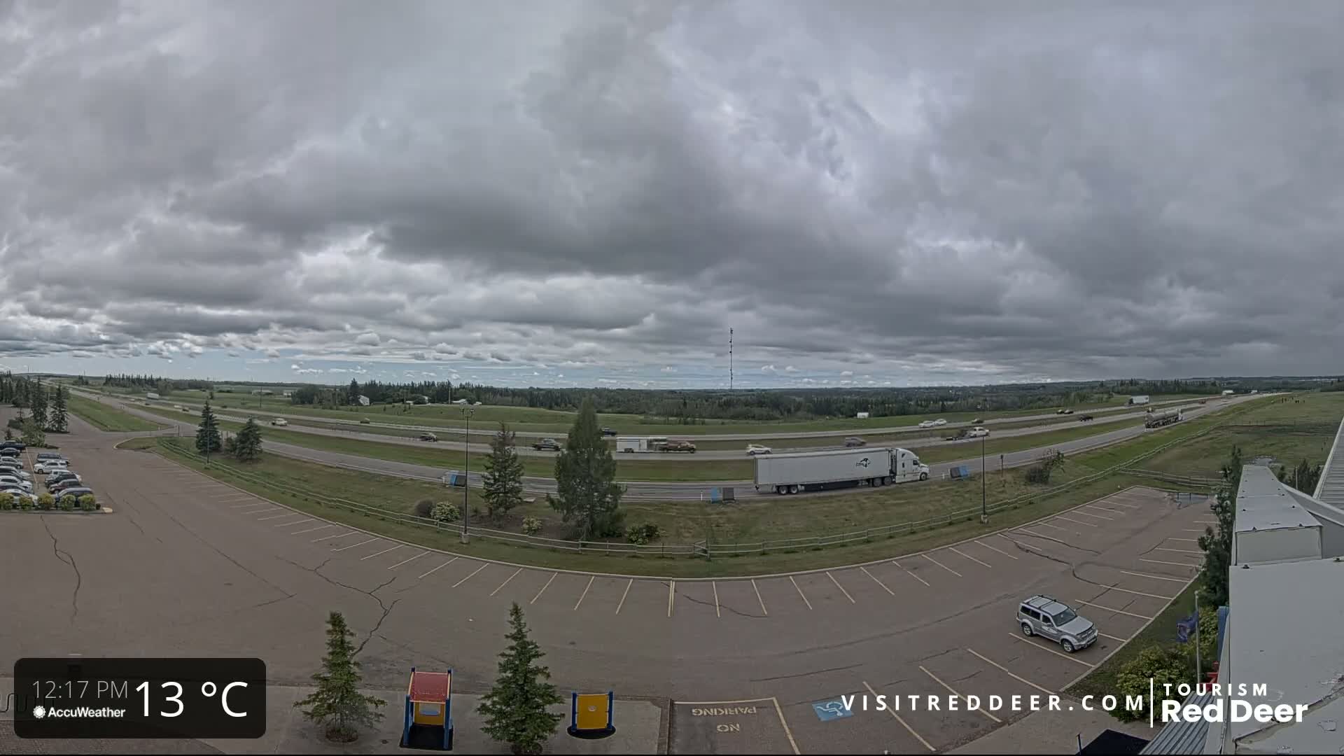 A mostly cloudy sky hangs over a highway with moderate traffic and an adjacent empty parking lot.