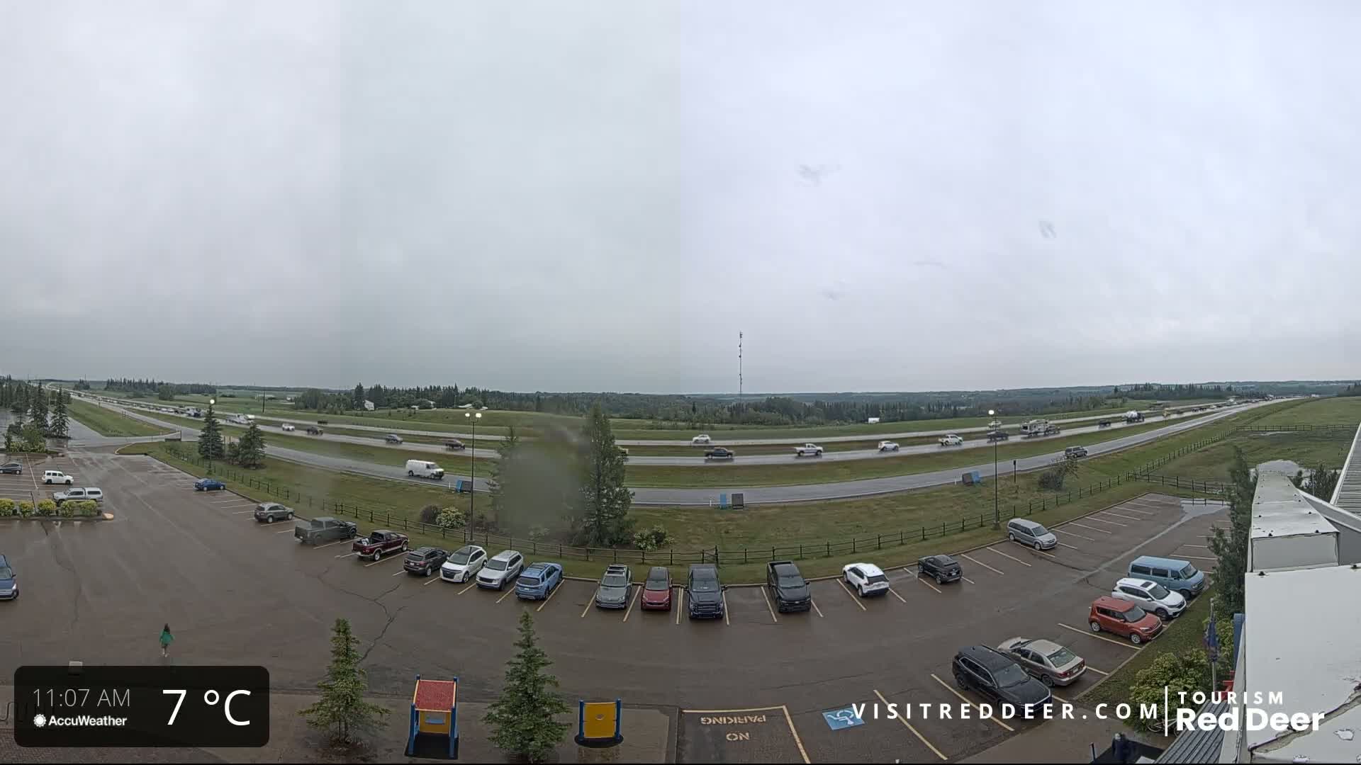 A partly cloudy, cool day shows a highway with moderate traffic and a mostly full parking lot next to it.