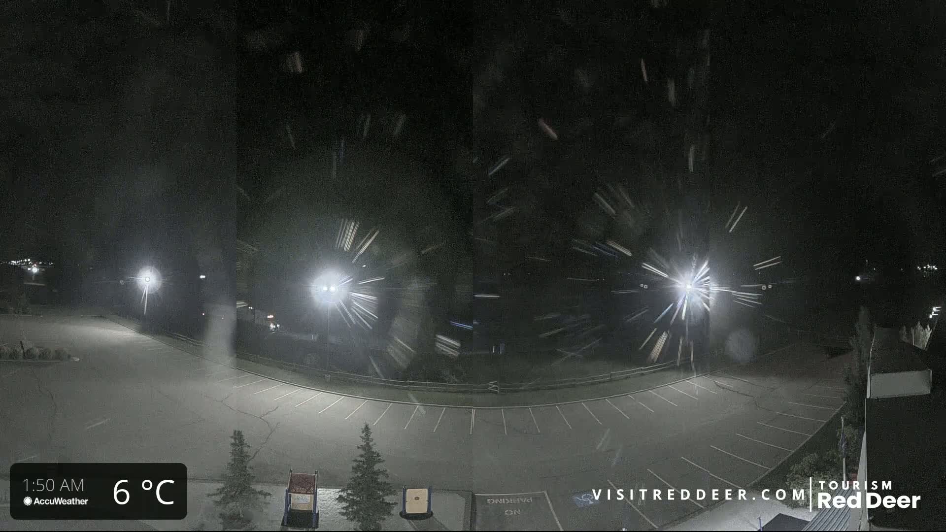 A nighttime, snow-filled parking lot is illuminated by several bright lights.