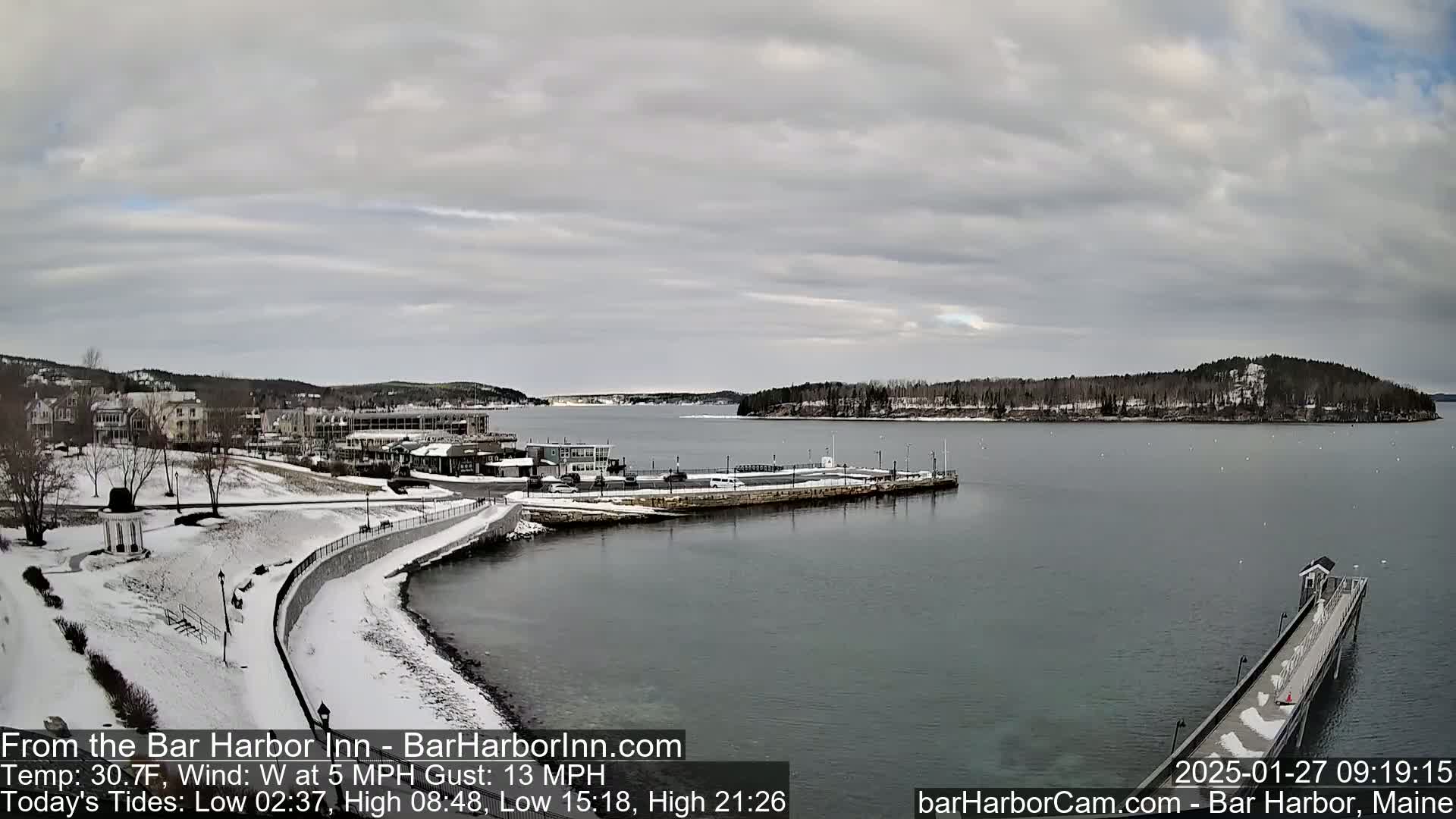 A snow-covered waterfront town overlooks a calm bay under a cloudy sky.