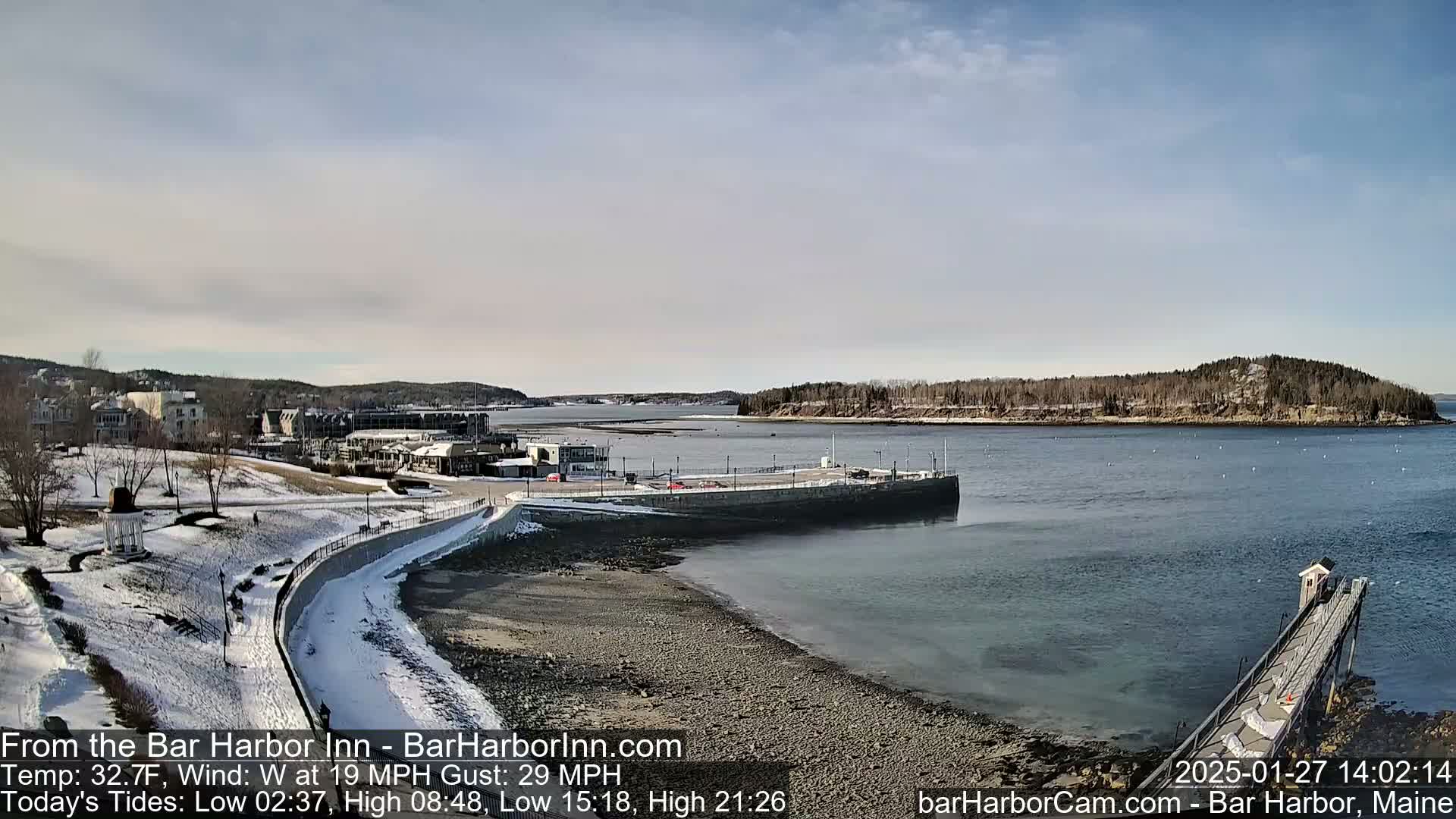 A snow-dusted waterfront scene shows a harbor with a town in the background under a mostly clear sky.