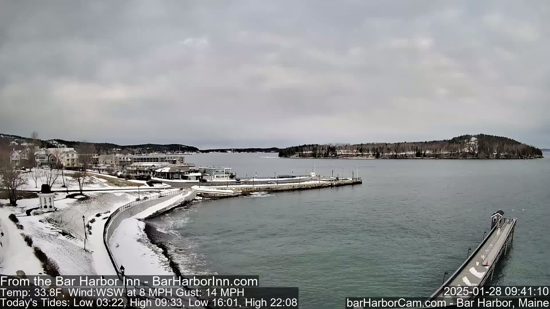 A snow-covered coastal town with a harbor and pier is visible under an overcast sky.