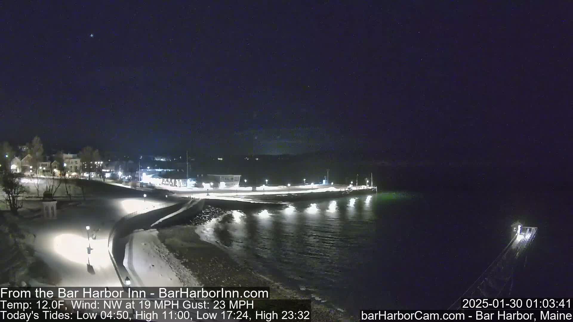 A nighttime view of a snow-covered harbor town under a dark, clear sky with a northwest wind blowing at 19 mph and gusting to 23 mph.